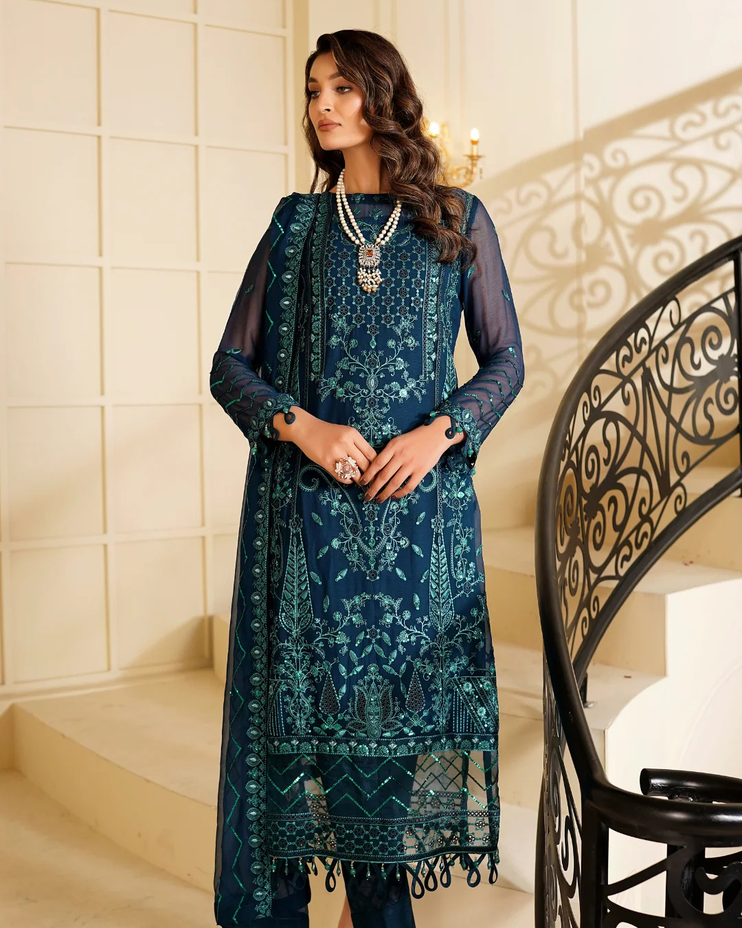 Woman wearing a teal embroidered dress with a decorative staircase in the background