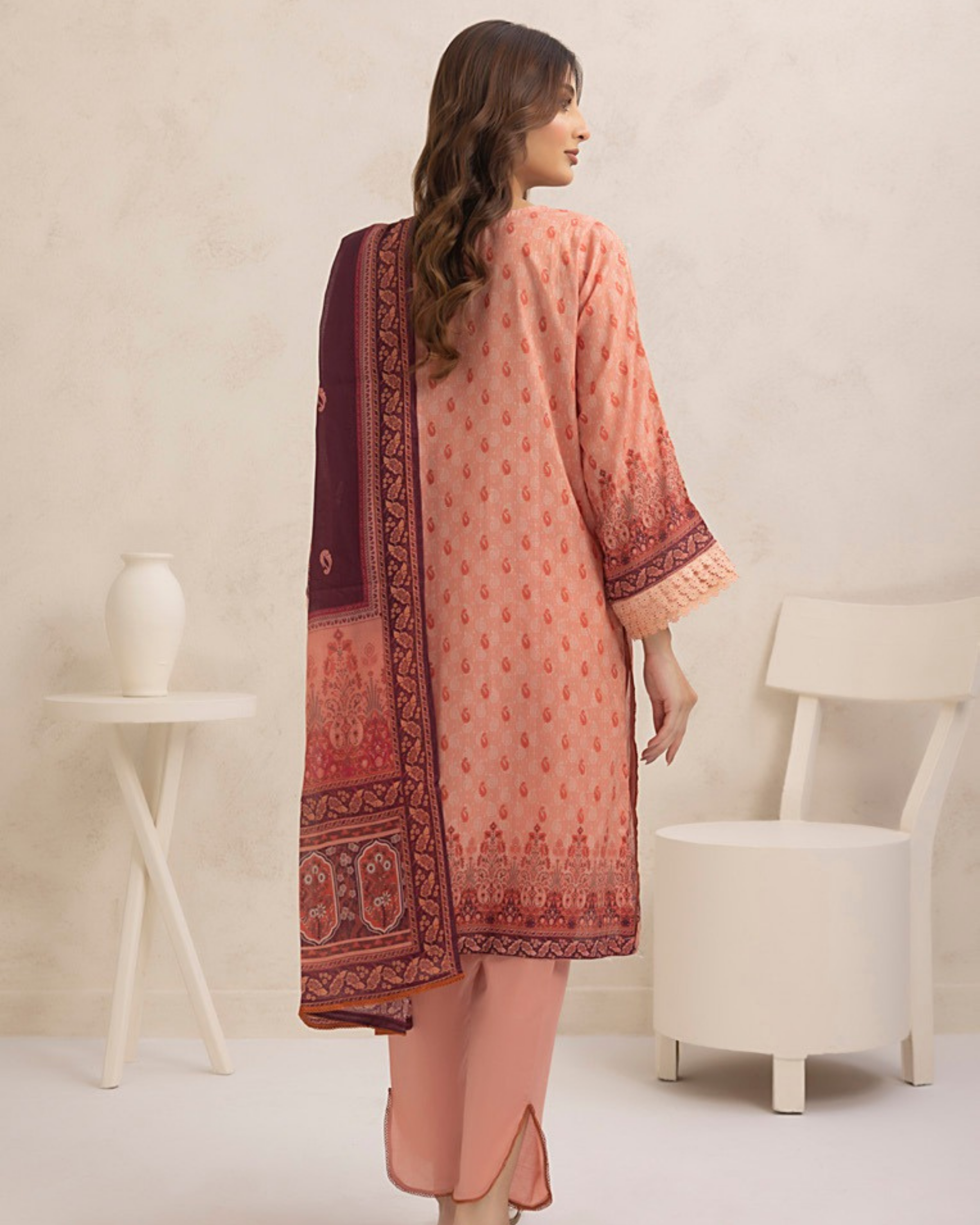 Woman wearing a pink and red traditional outfit with a matching dupatta in a minimalistic setting.