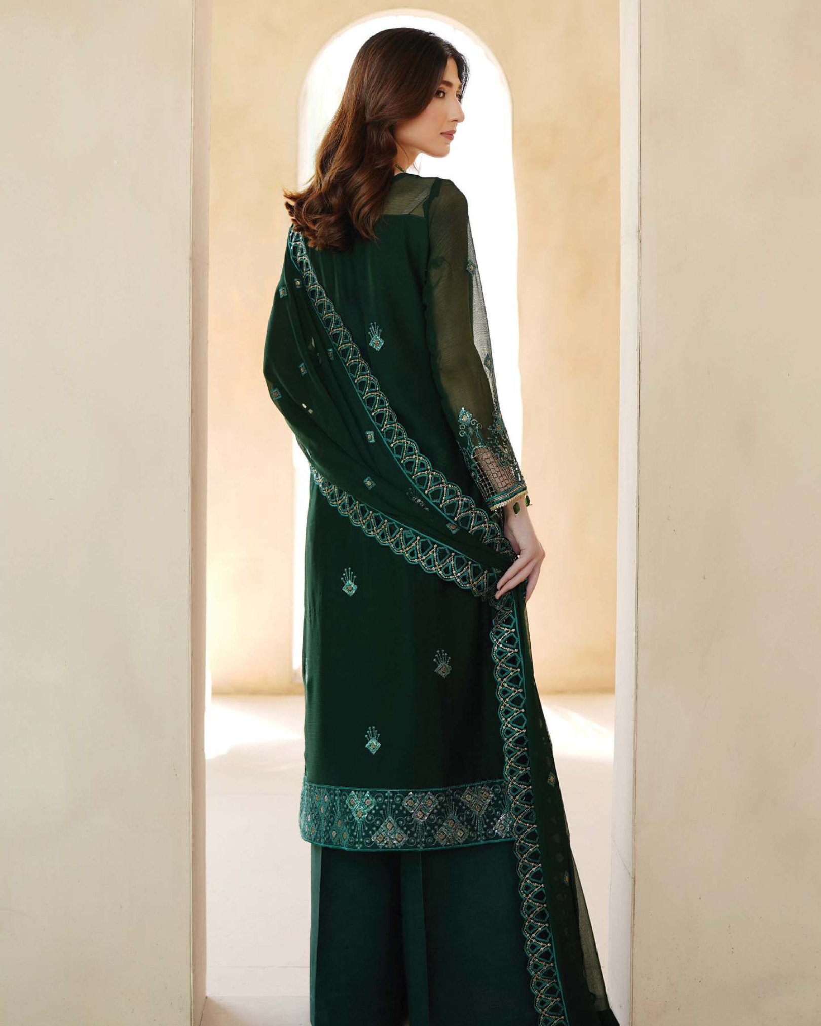 Woman wearing a dark green embroidered traditional outfit in a neutral setting