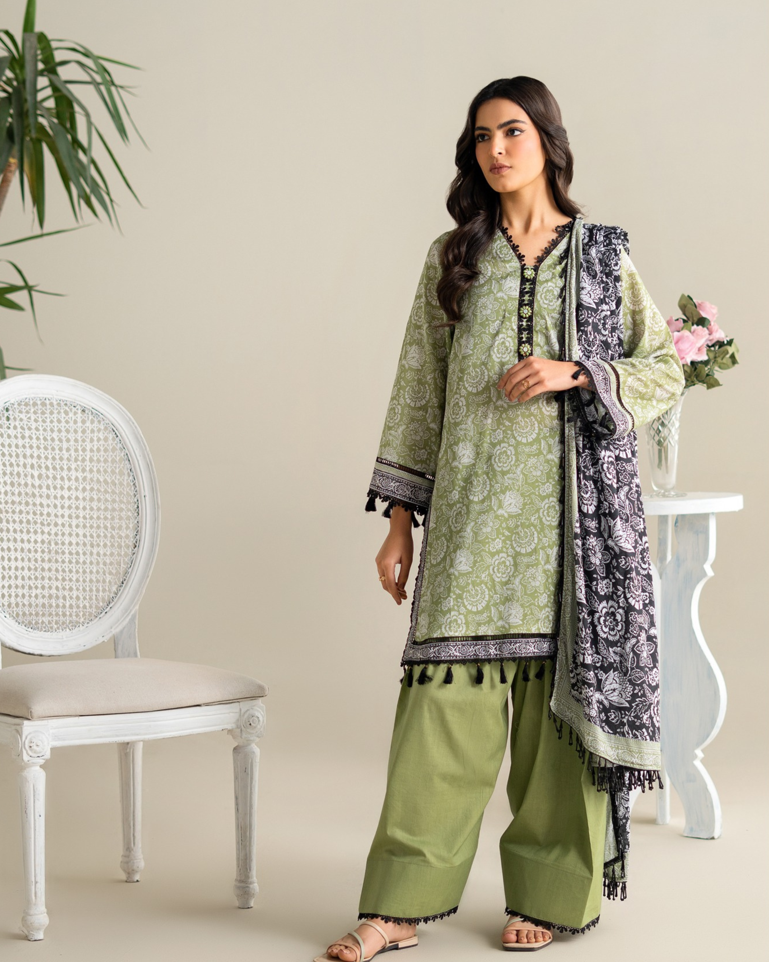 Woman wearing a green traditional outfit with a patterned scarf in a minimalistic setting.