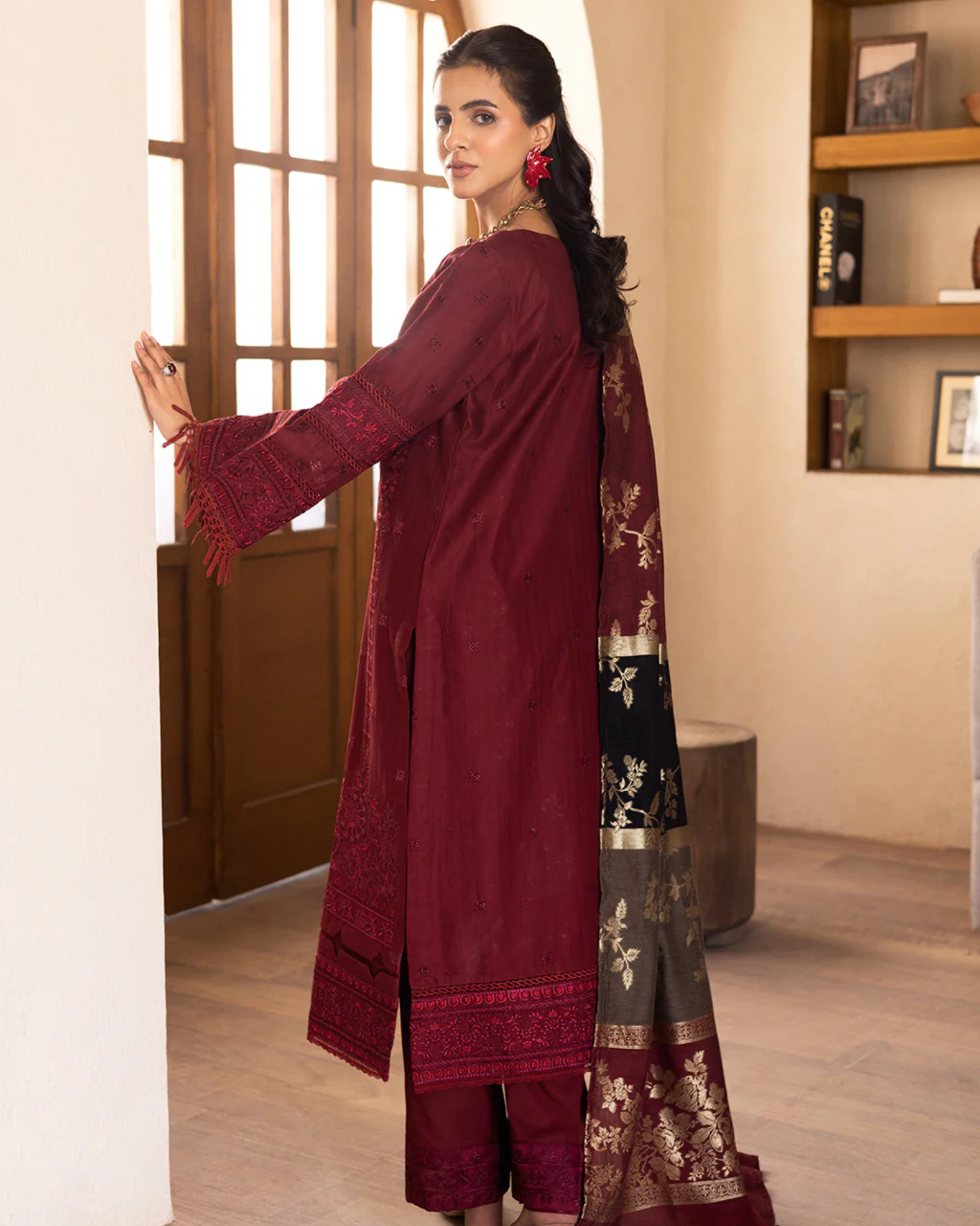Woman wearing a maroon traditional outfit with a floral dupatta in a room.