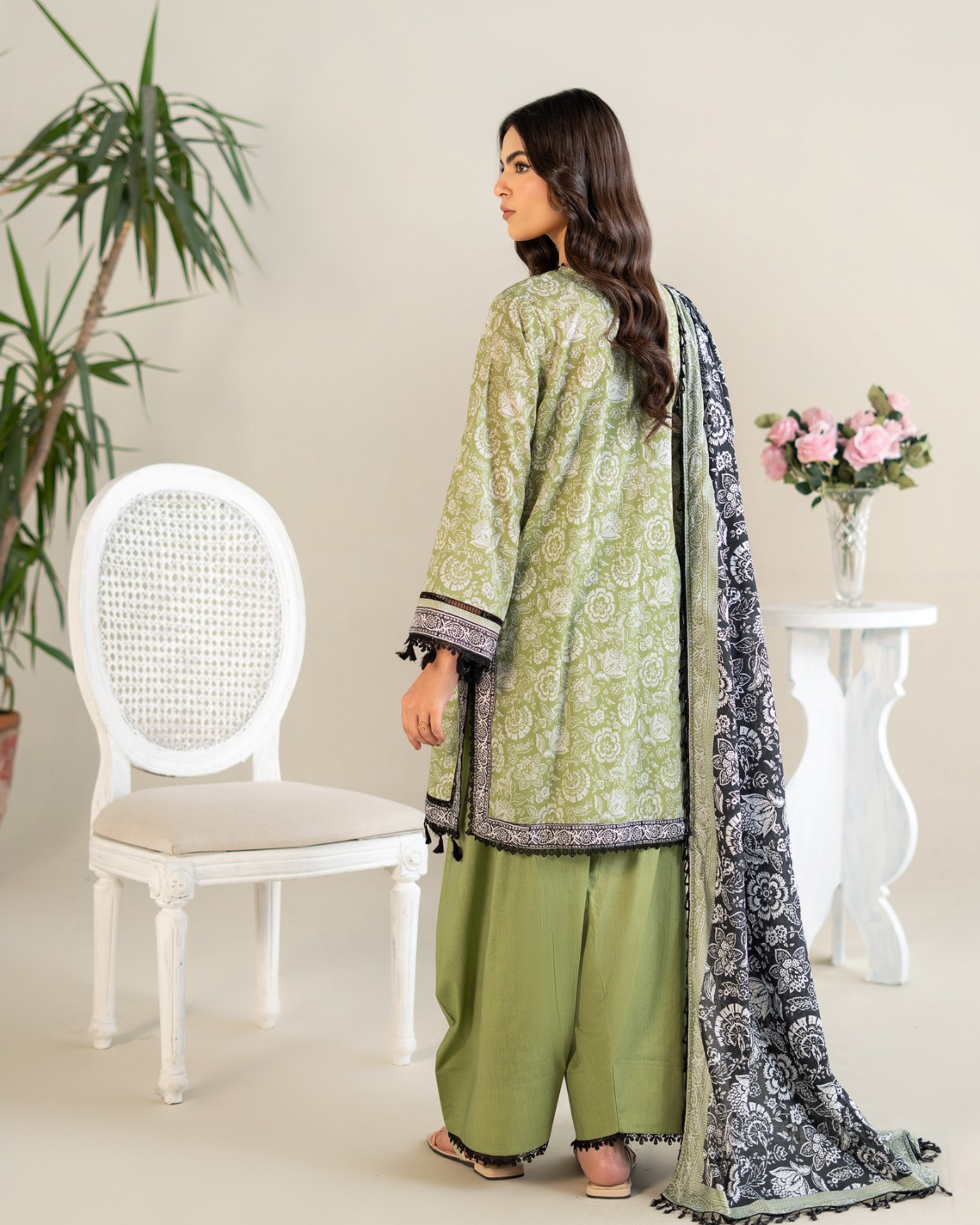 Woman in a green traditional outfit with a black and white dupatta in a minimalistic room.