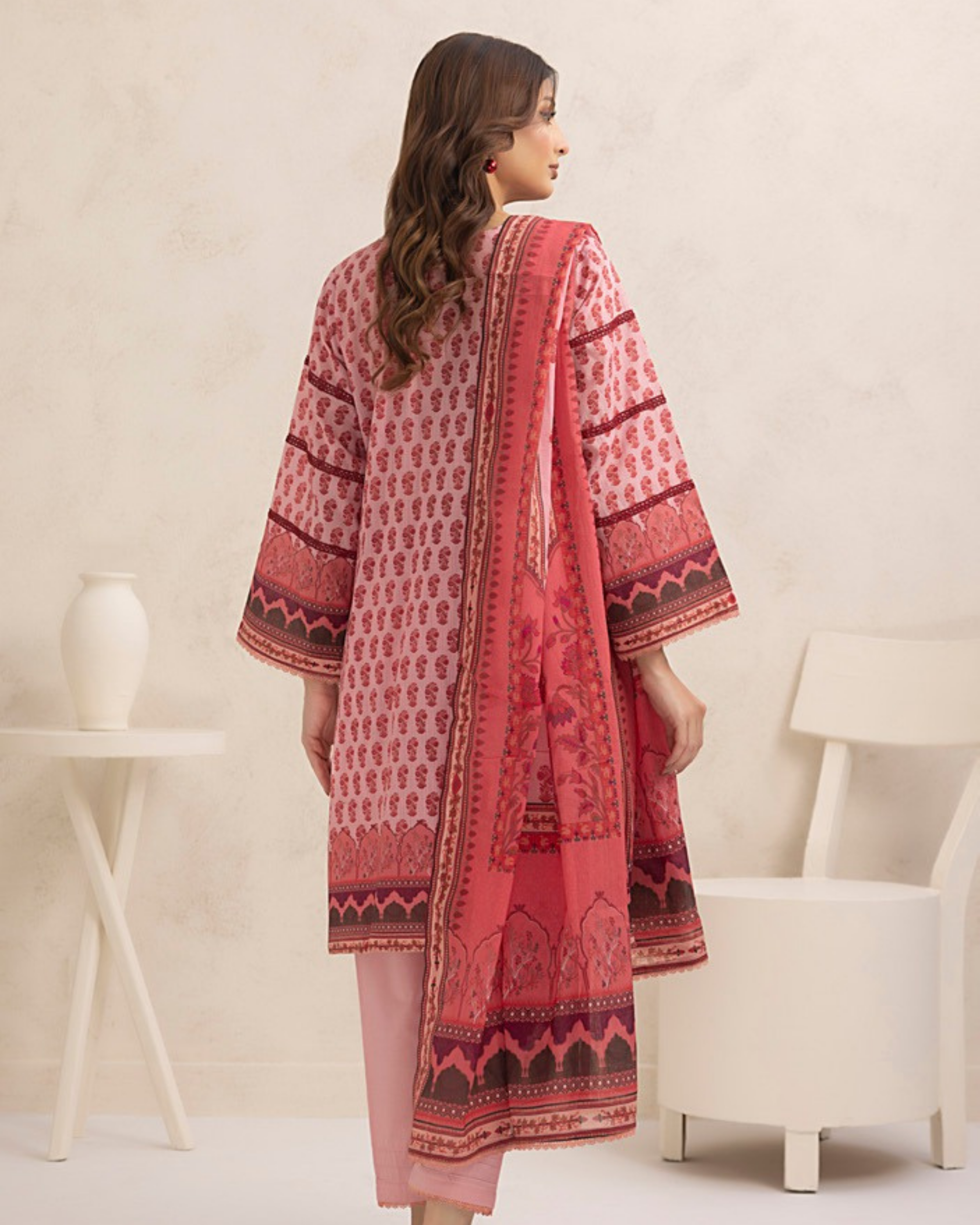 Woman wearing a red and pink patterned kurta with a white chair and table in the background