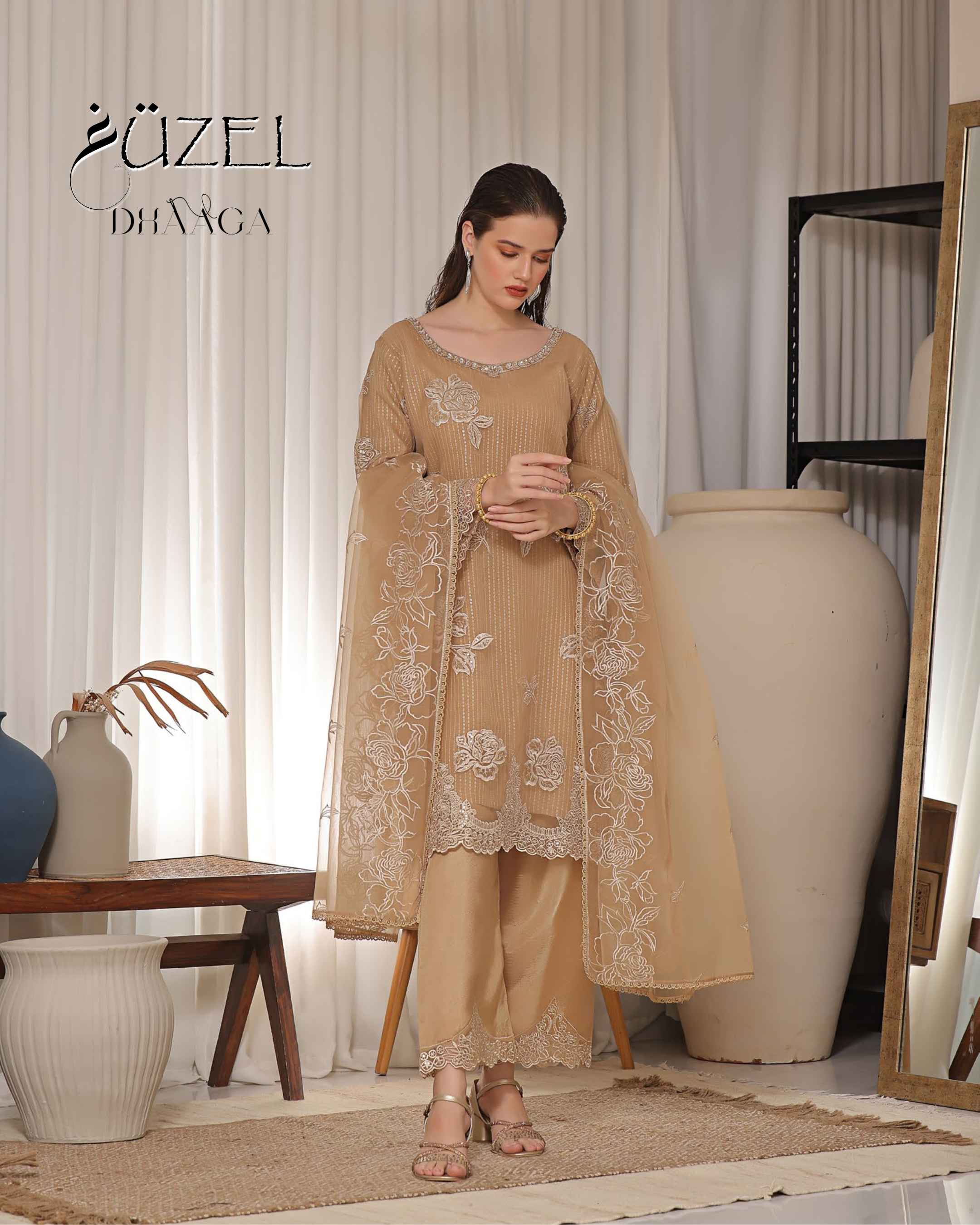Woman in a beige embroidered outfit standing in a room with decor elements.