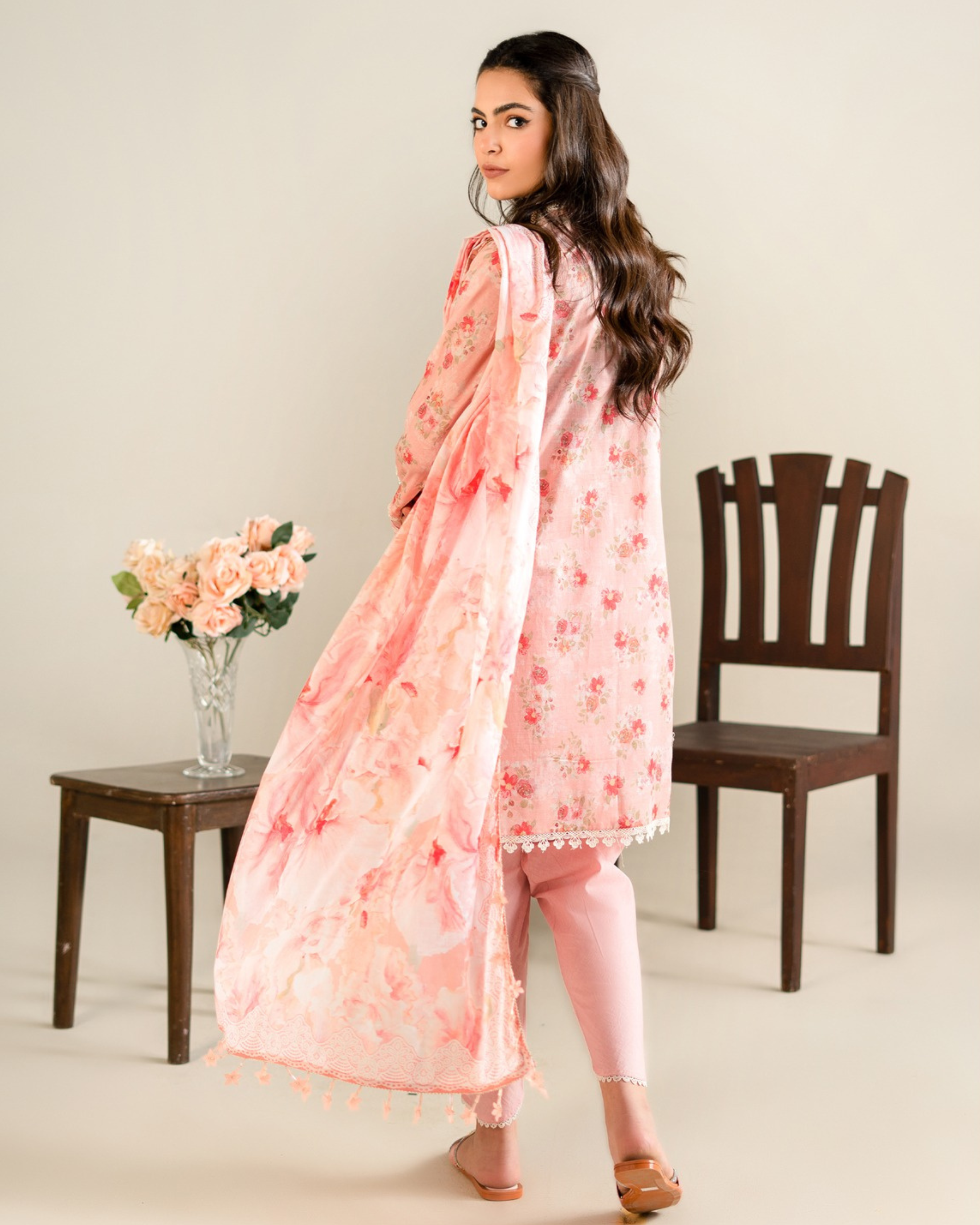 Woman wearing a pink floral outfit with a vase of flowers and chair in the background