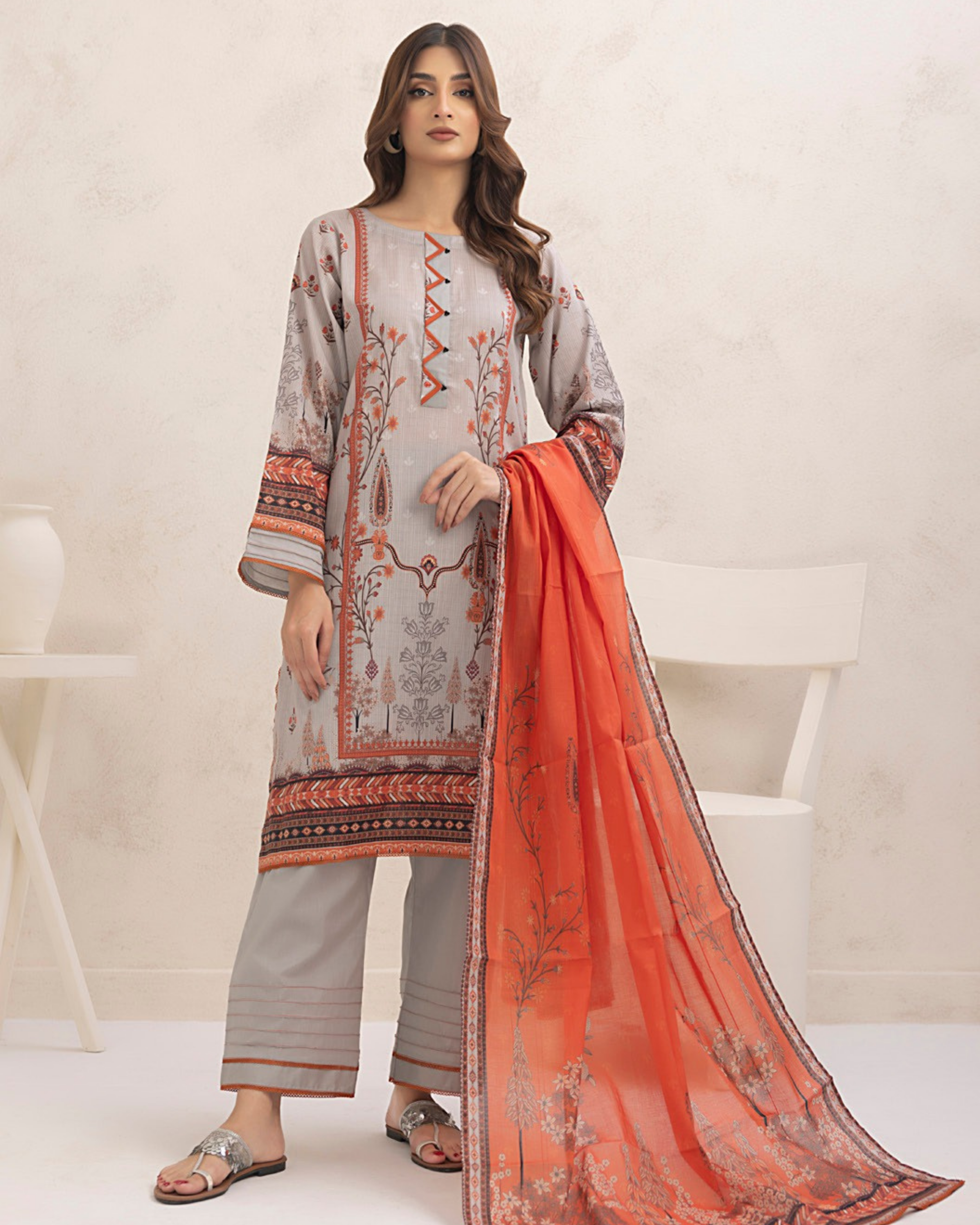 Woman wearing a traditional outfit with a gray and orange patterned dress and orange dupatta on a white background