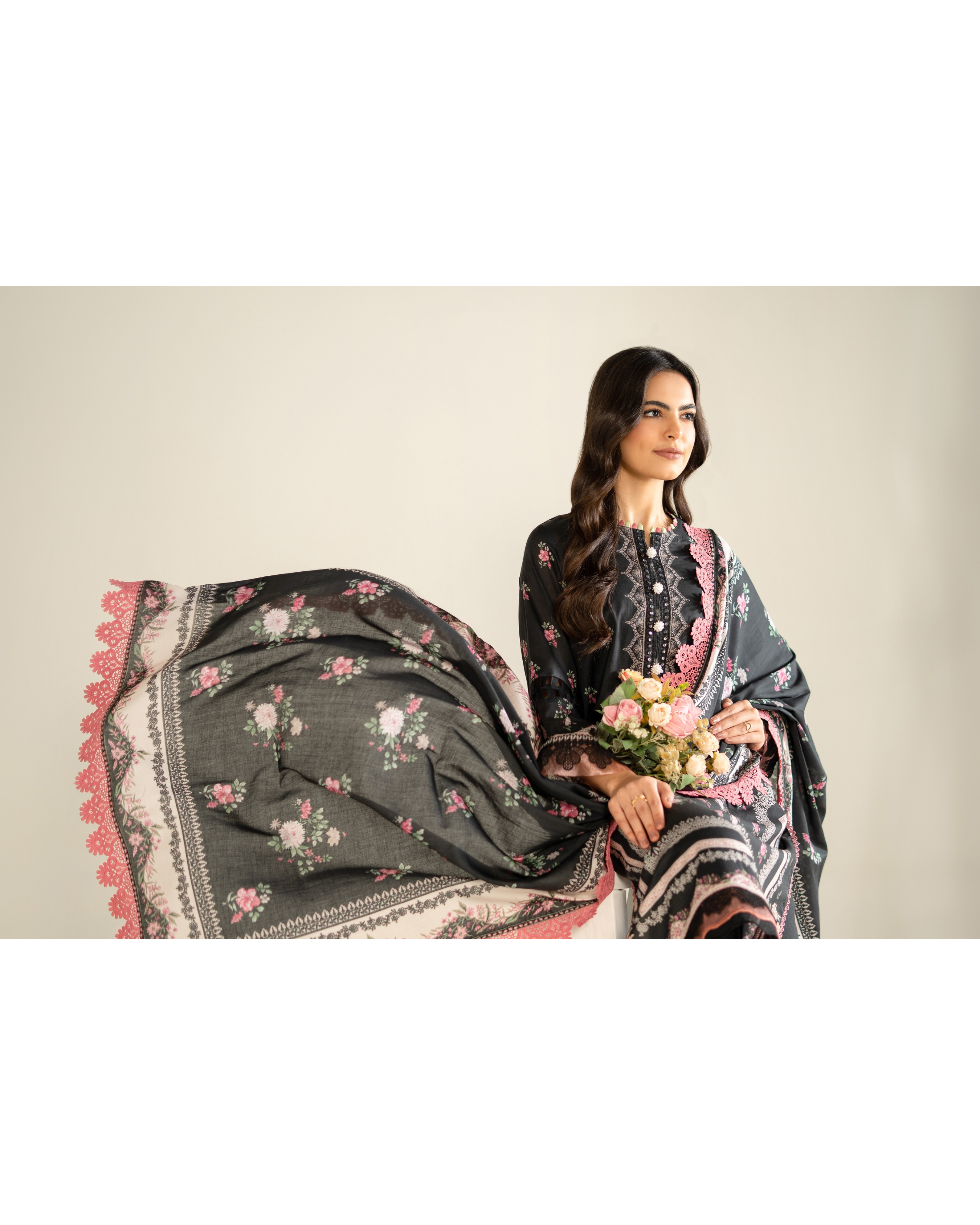 Woman holding a floral-patterned shawl against a plain background