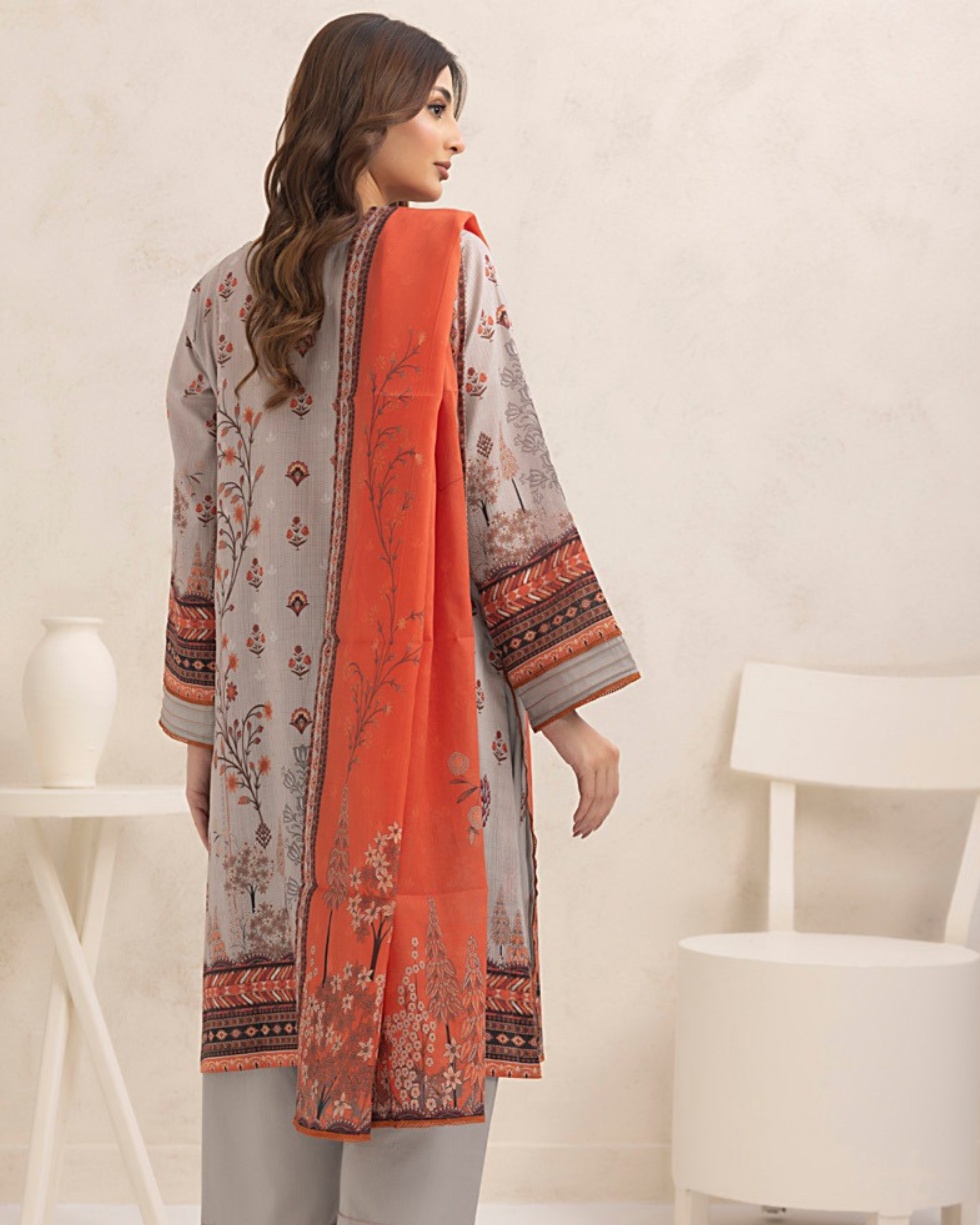 Woman wearing a patterned shirt with an orange dupatta in a minimalistic setting
