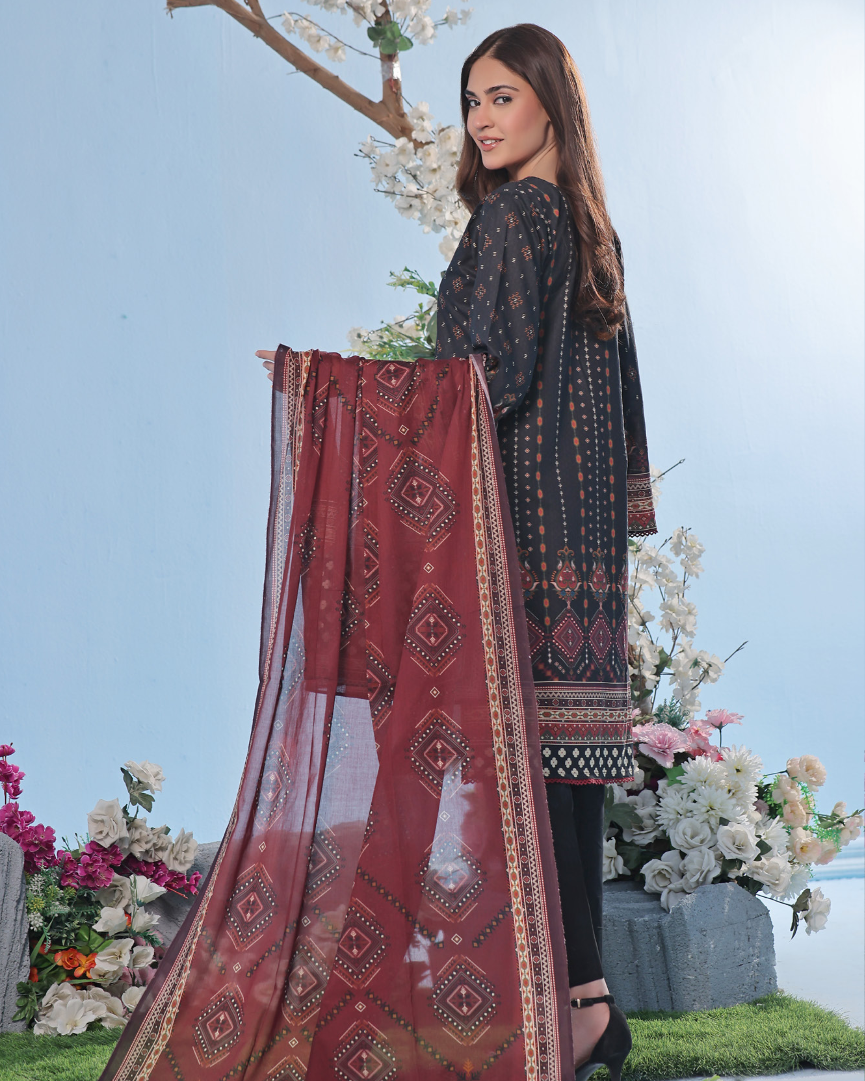 Woman holding a red patterned dupatta with floral decorations in the background