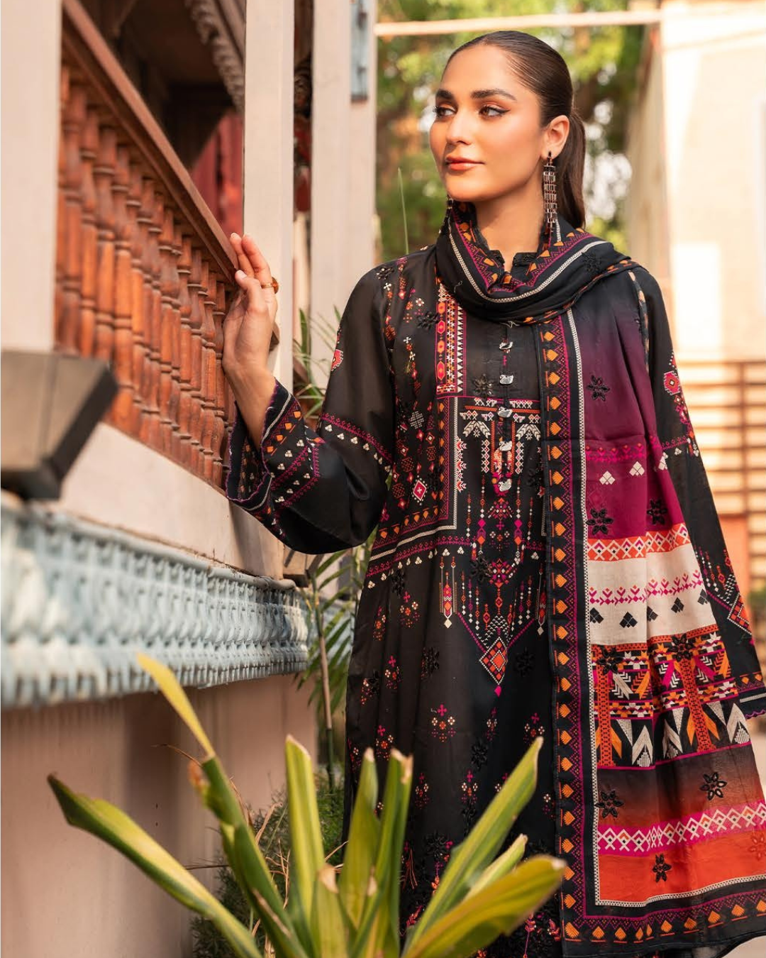Woman wearing a black embroidered outfit with a colorful dupatta, standing outdoors.
