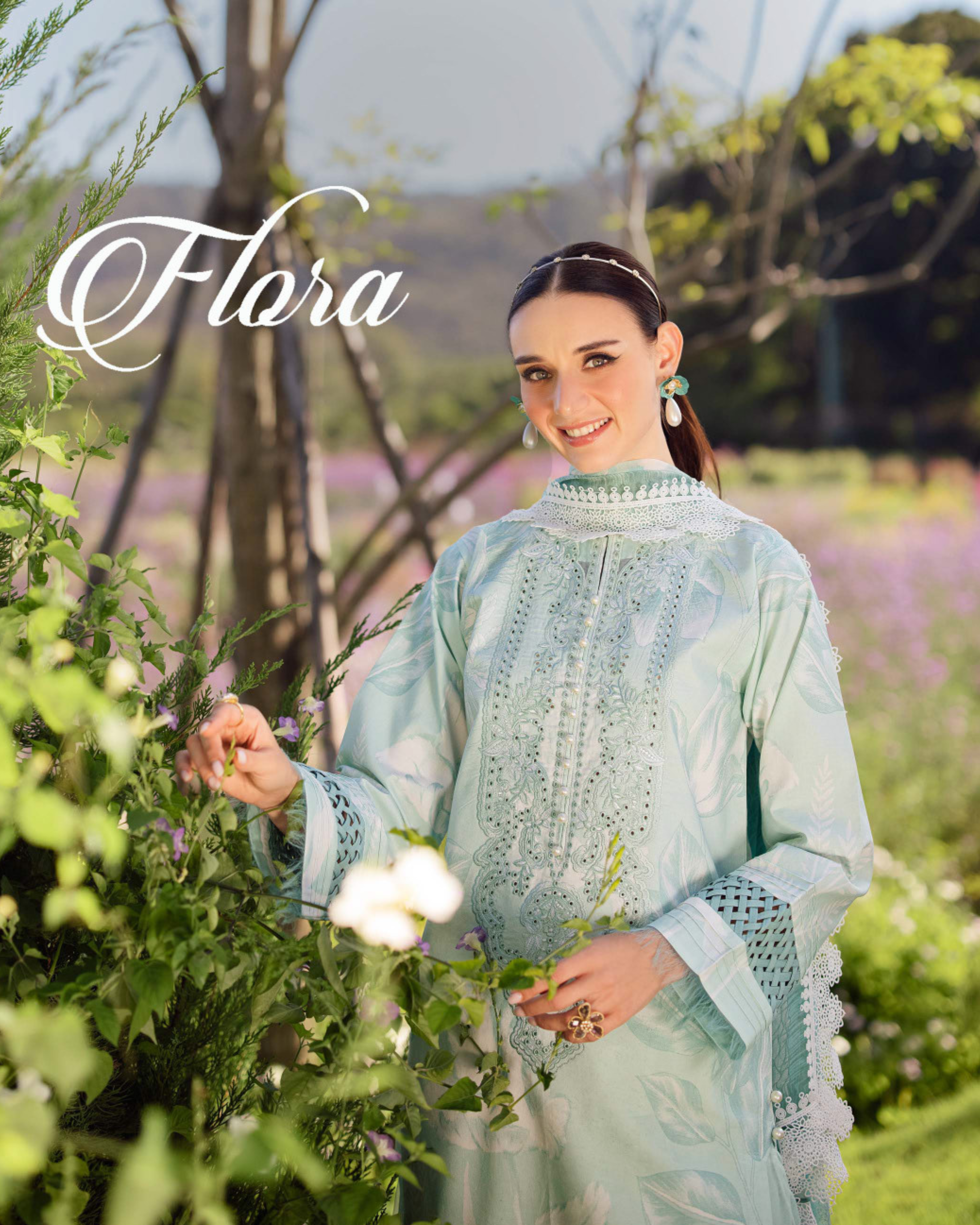 Woman in a light blue embroidered outfit standing in a garden with 'Flora' branding.