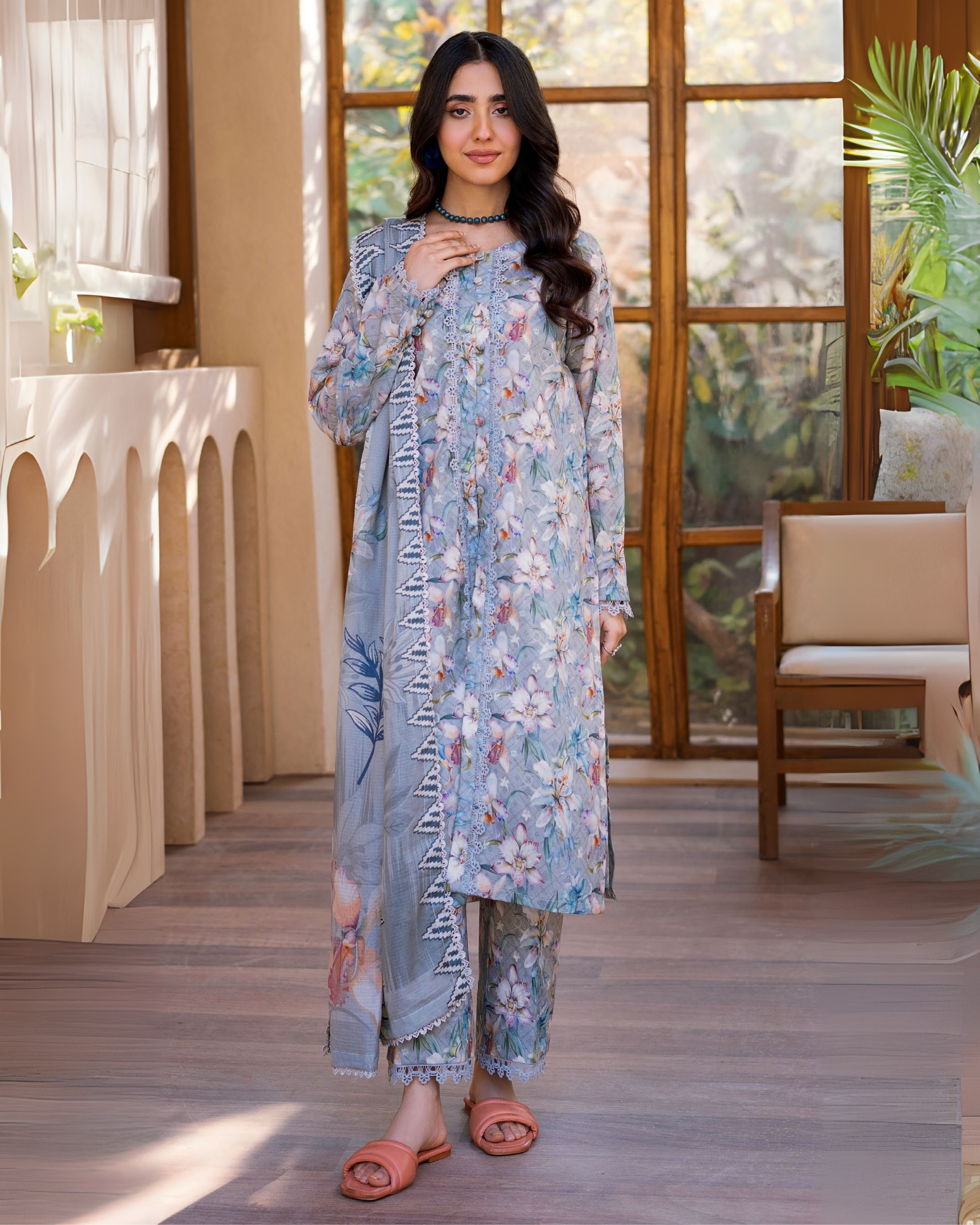 Woman wearing a floral outfit standing in a well-lit room with large windows.