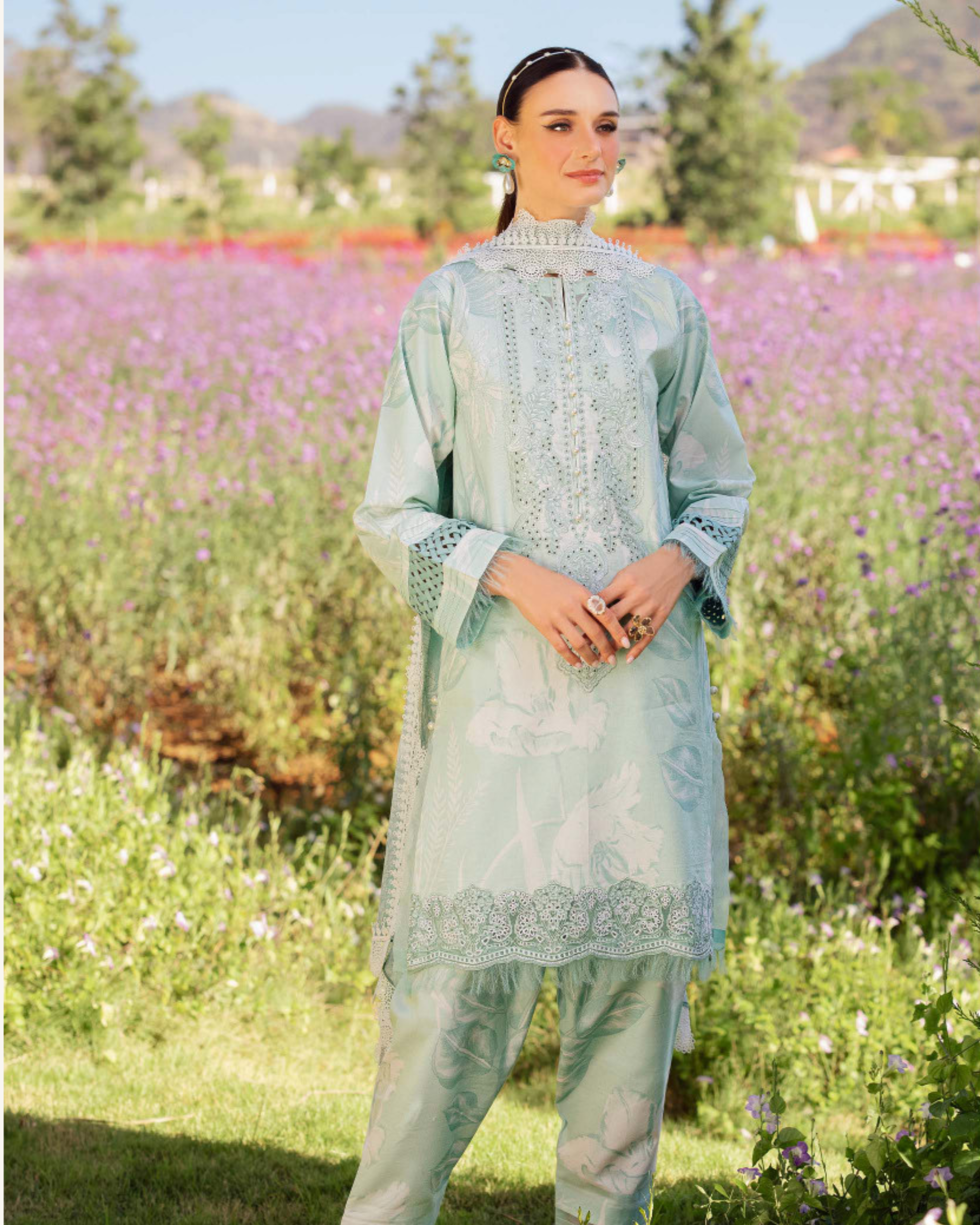 Woman in a light blue embroidered outfit standing in a field of flowers