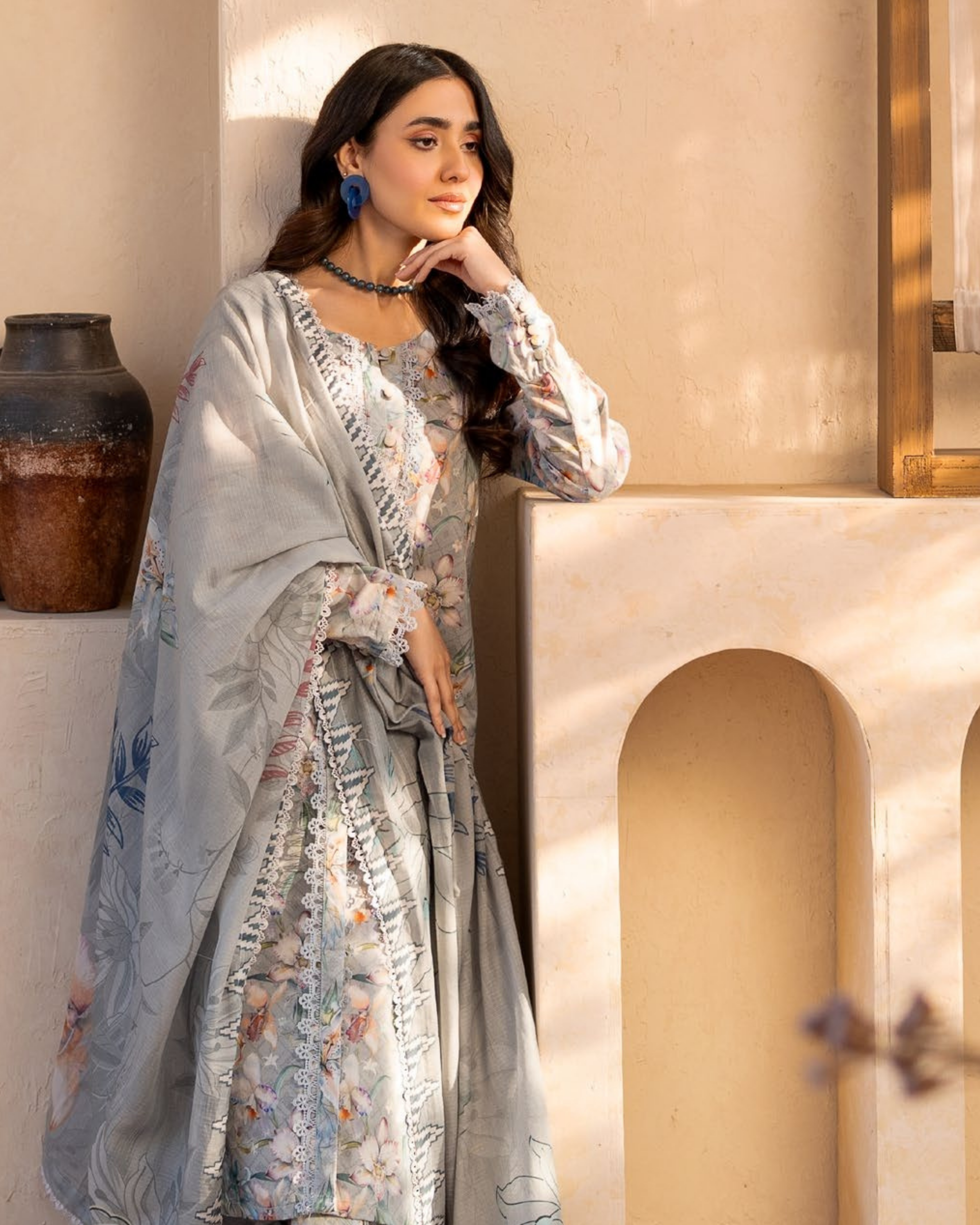 Woman in a floral dress standing against a decorative wall.