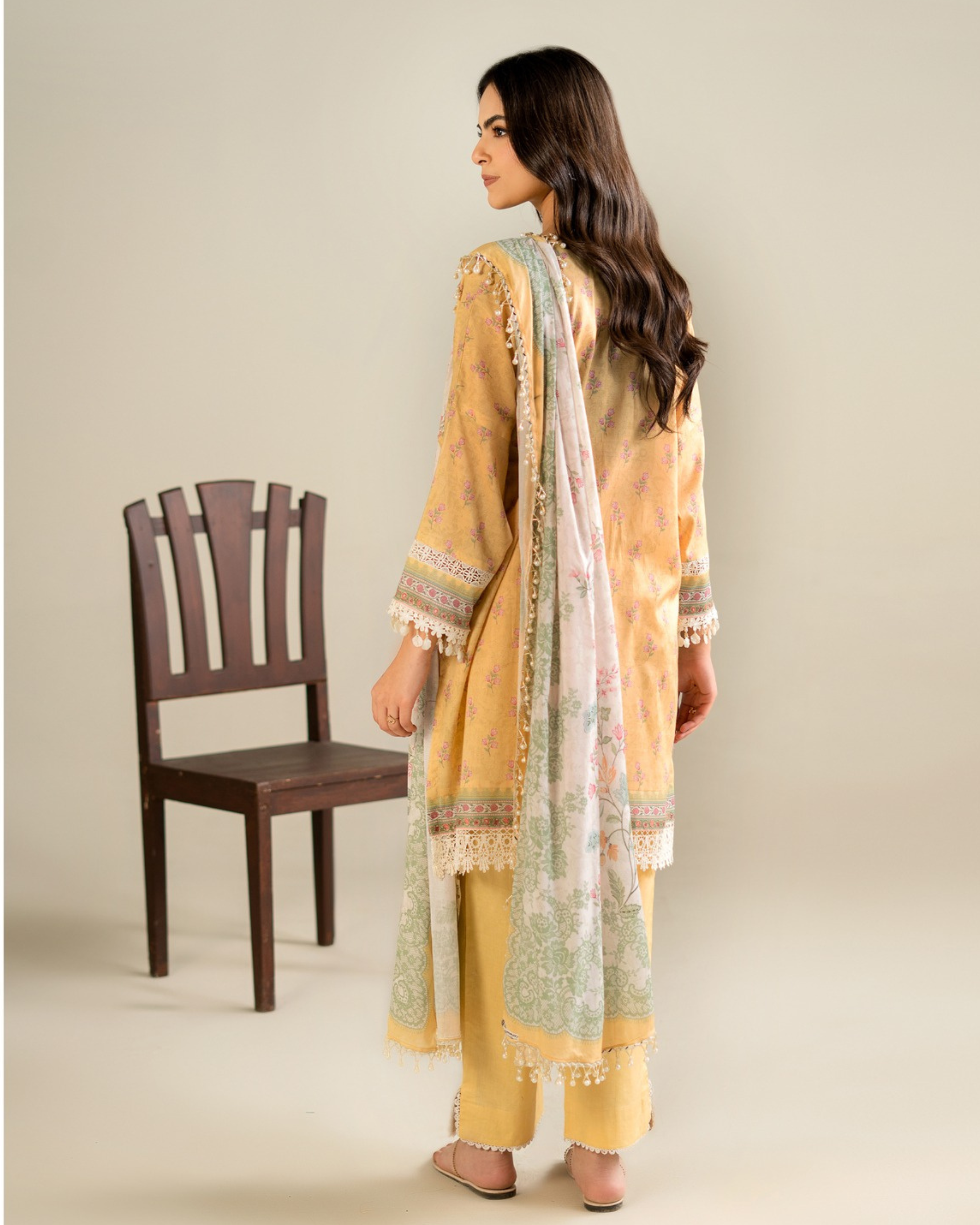 Woman wearing a yellow and green traditional outfit with a chair in the background