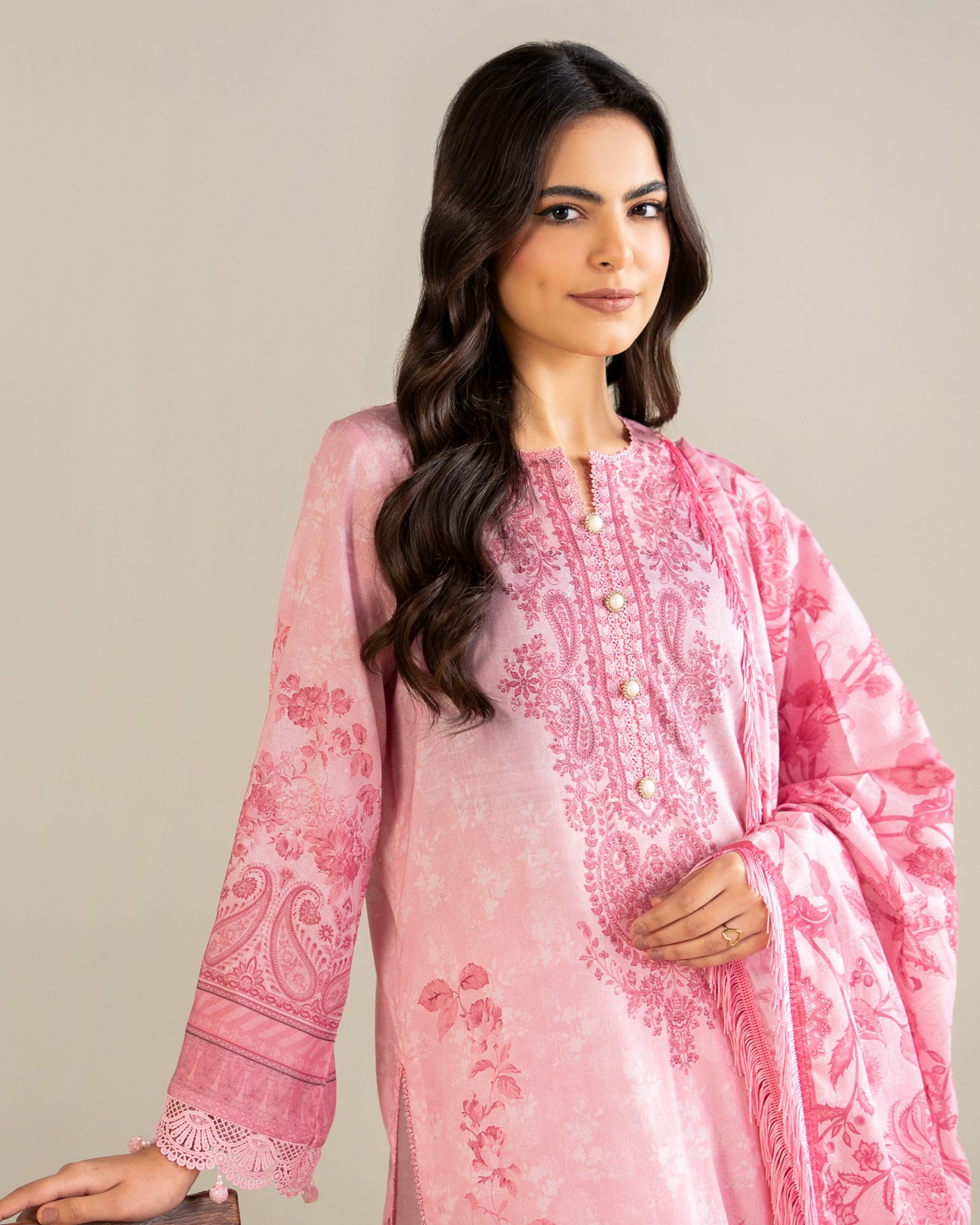 Woman wearing a pink embroidered traditional outfit against a plain background