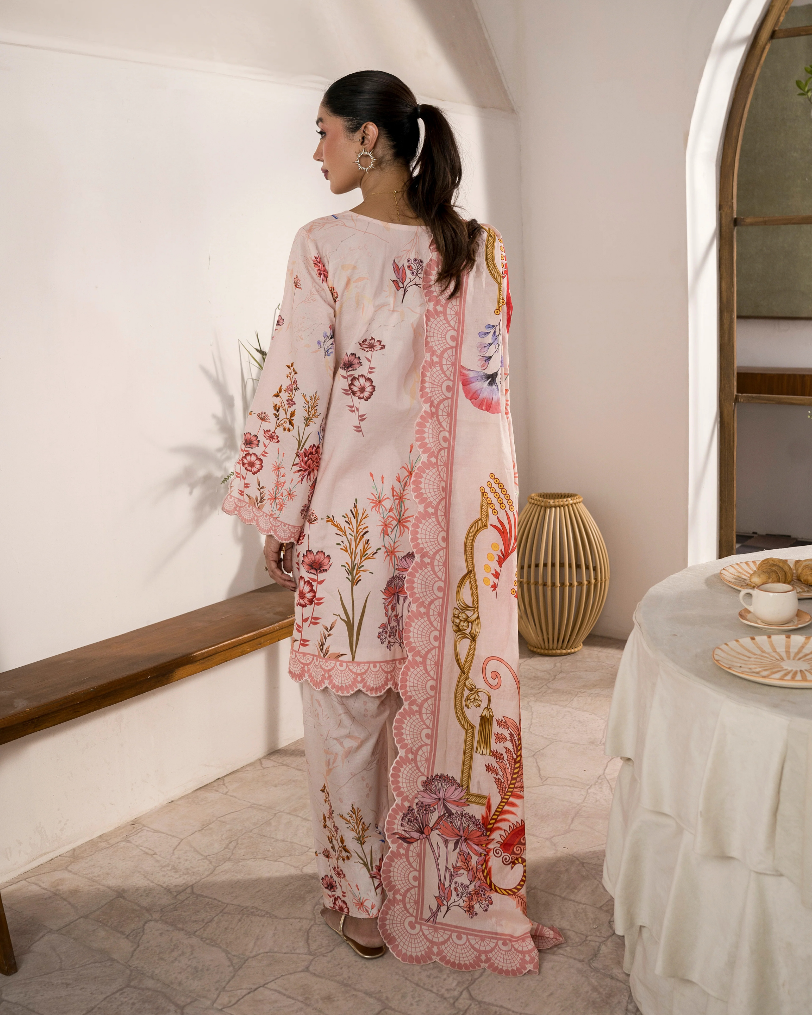 Woman wearing a floral embroidered outfit in a room with a table and decorative items.
