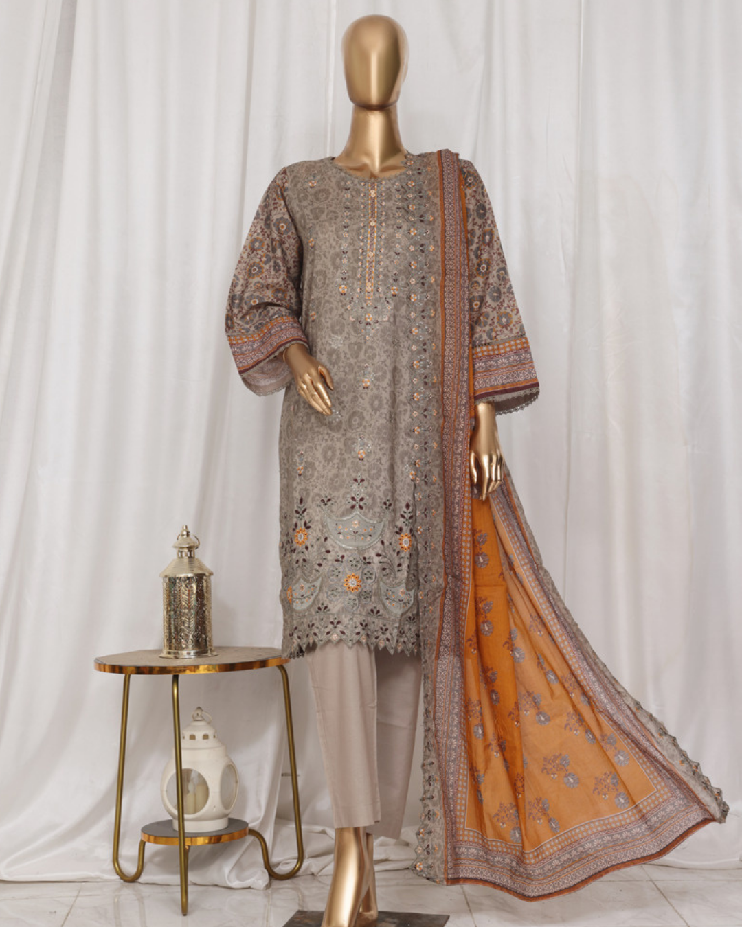 Mannequin wearing a traditional outfit with a patterned shirt and orange dupatta against a white curtain background.