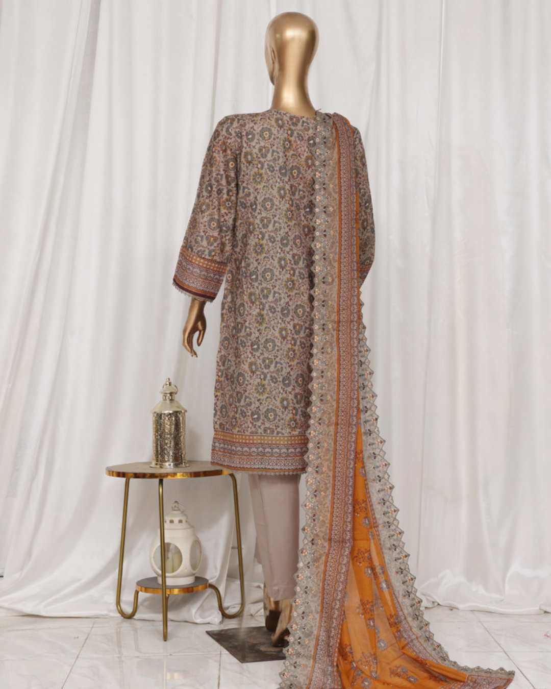 Mannequin wearing a patterned dress with an orange dupatta against a white curtain background