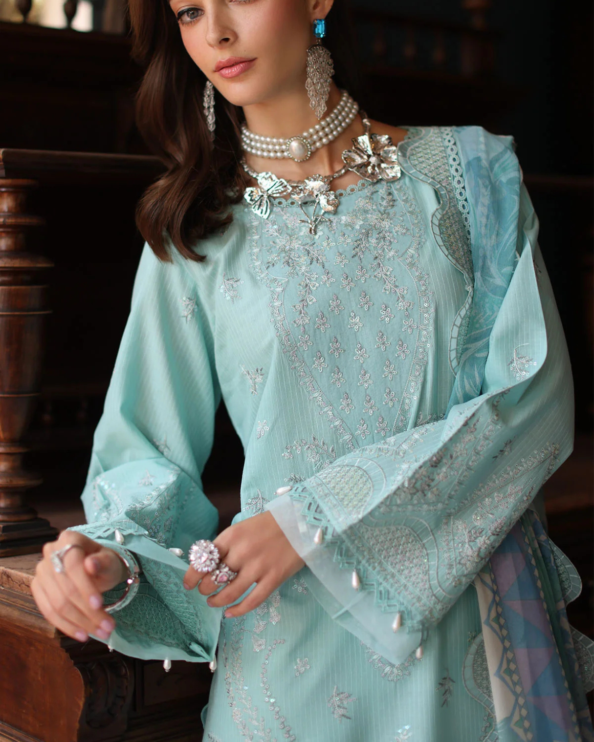 Woman wearing a light blue embroidered dress with jewelry in an indoor setting