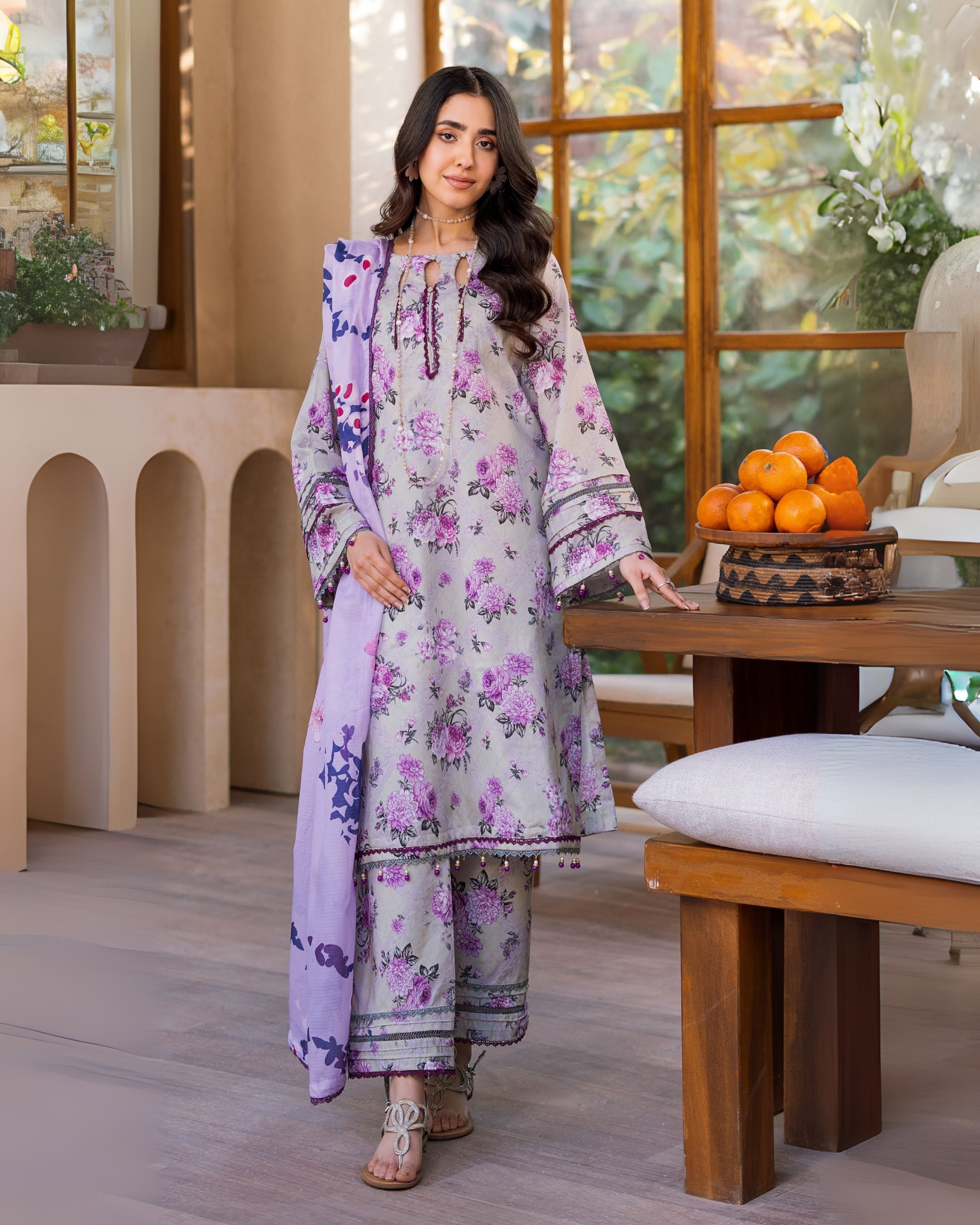 Woman in a floral dress standing in a room with wooden furniture and decorative items.