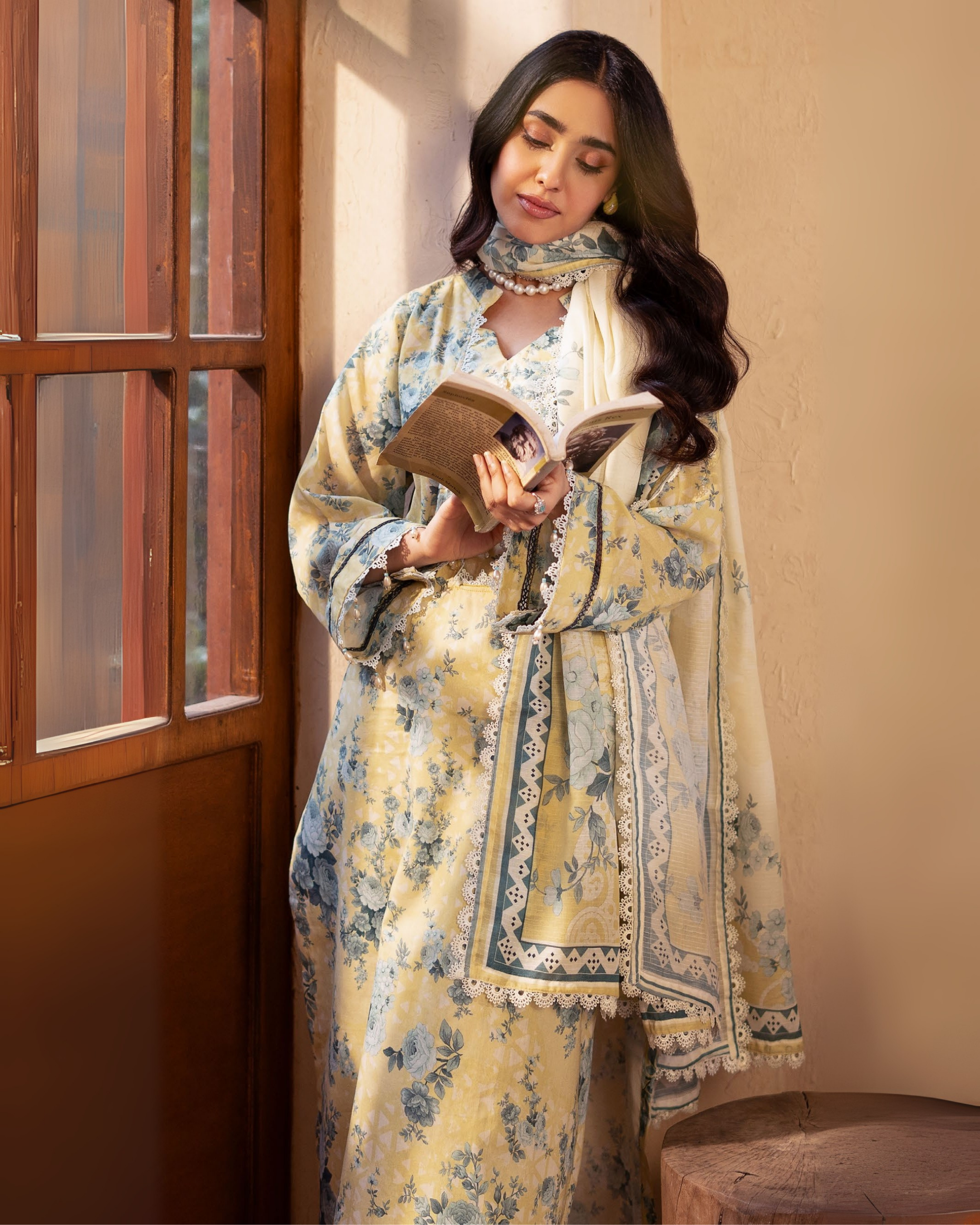Woman in a floral outfit holding a book in a sunlit room.
