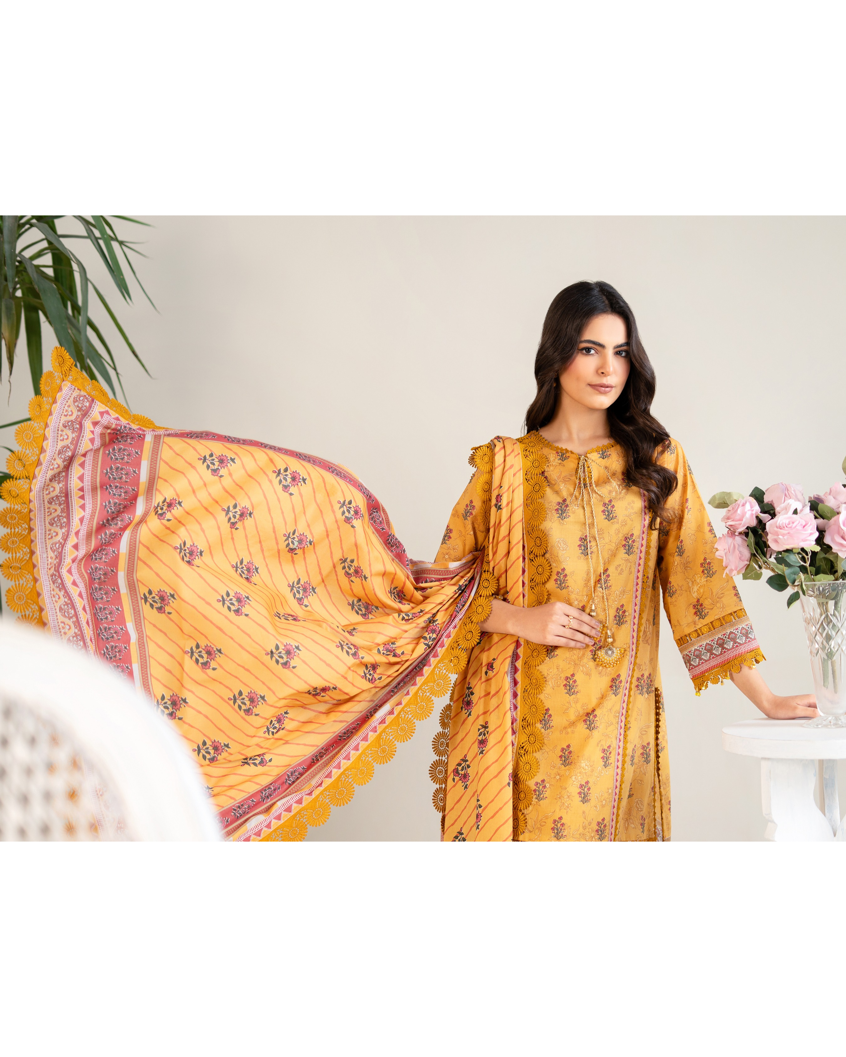 Woman wearing a yellow traditional outfit with a patterned dupatta in a minimalistic setting.