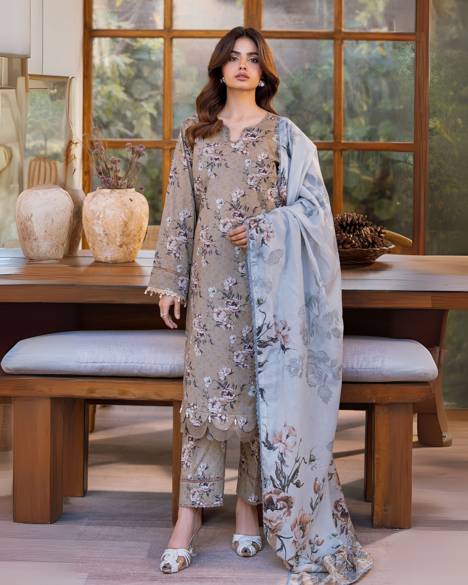 Woman in a floral dress standing in a room with wooden furniture and decorative items.