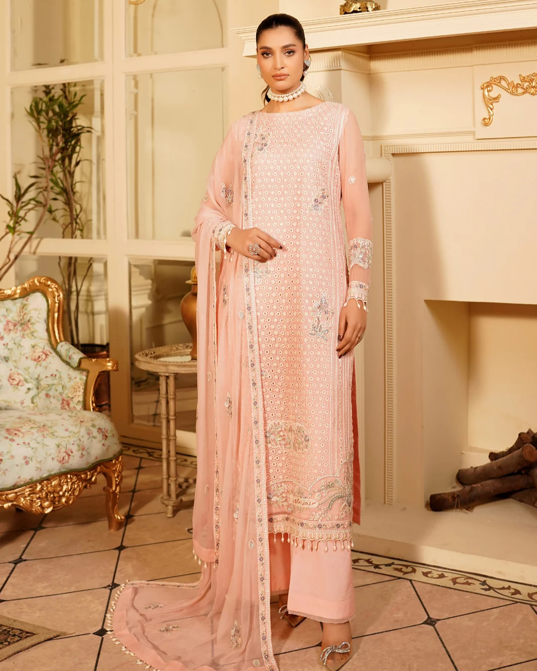 Woman in a pink traditional outfit standing in an elegant room with decorative elements.
