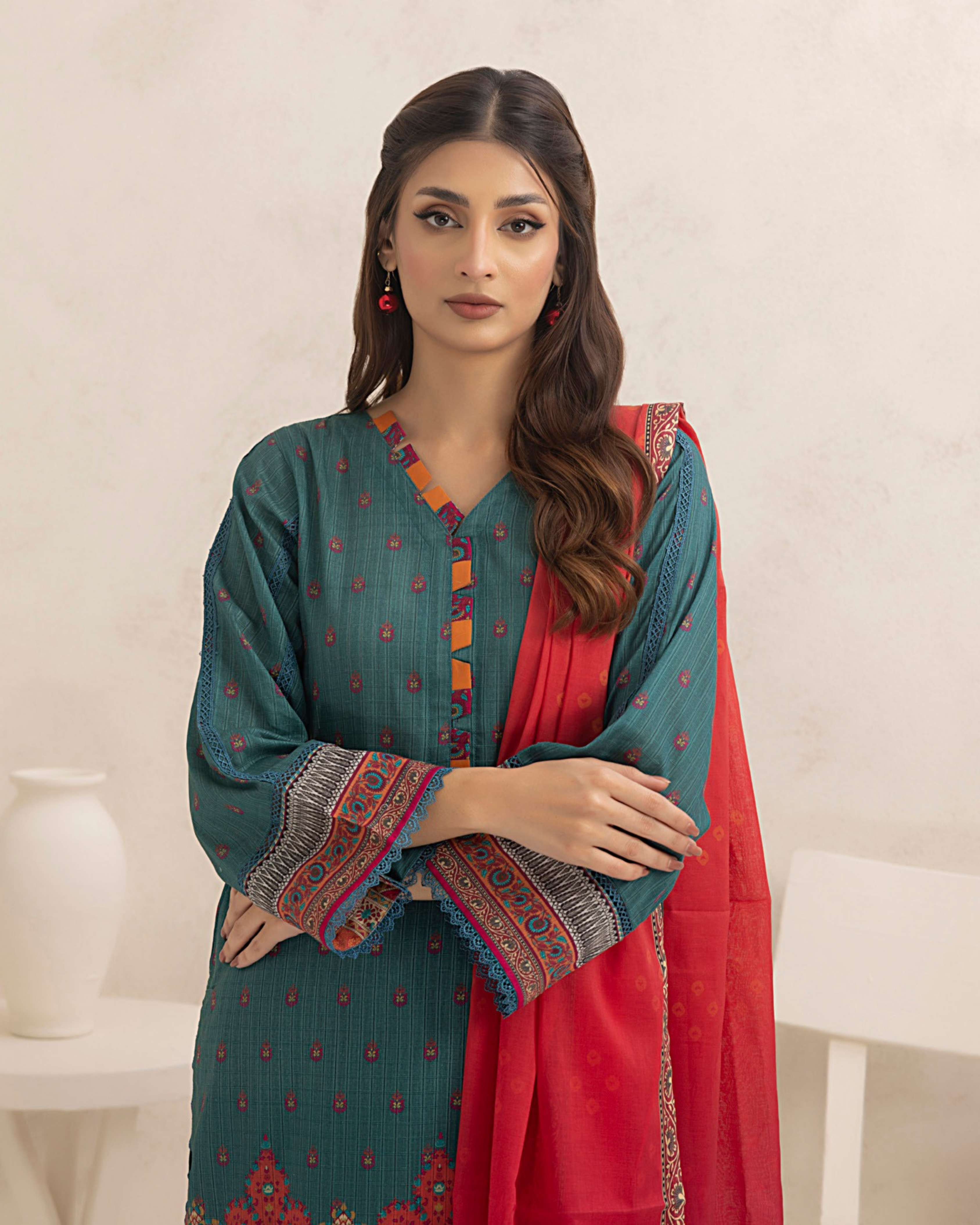 Woman wearing a teal and red traditional outfit with intricate patterns on a white background
