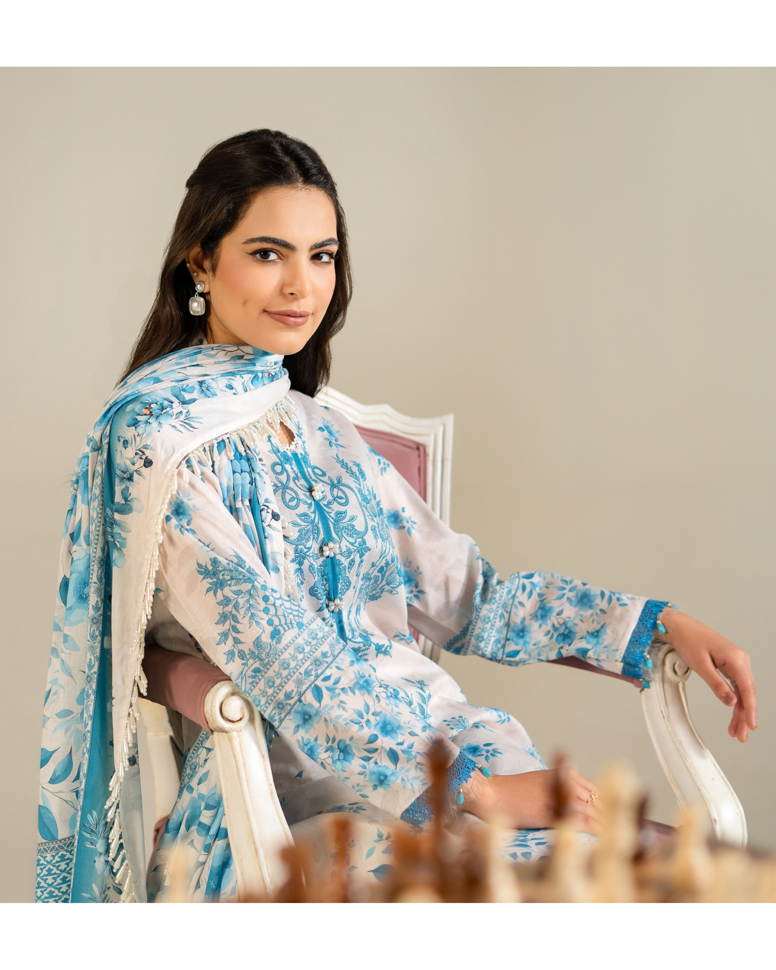 Woman in a blue and white floral outfit sitting on a chair.