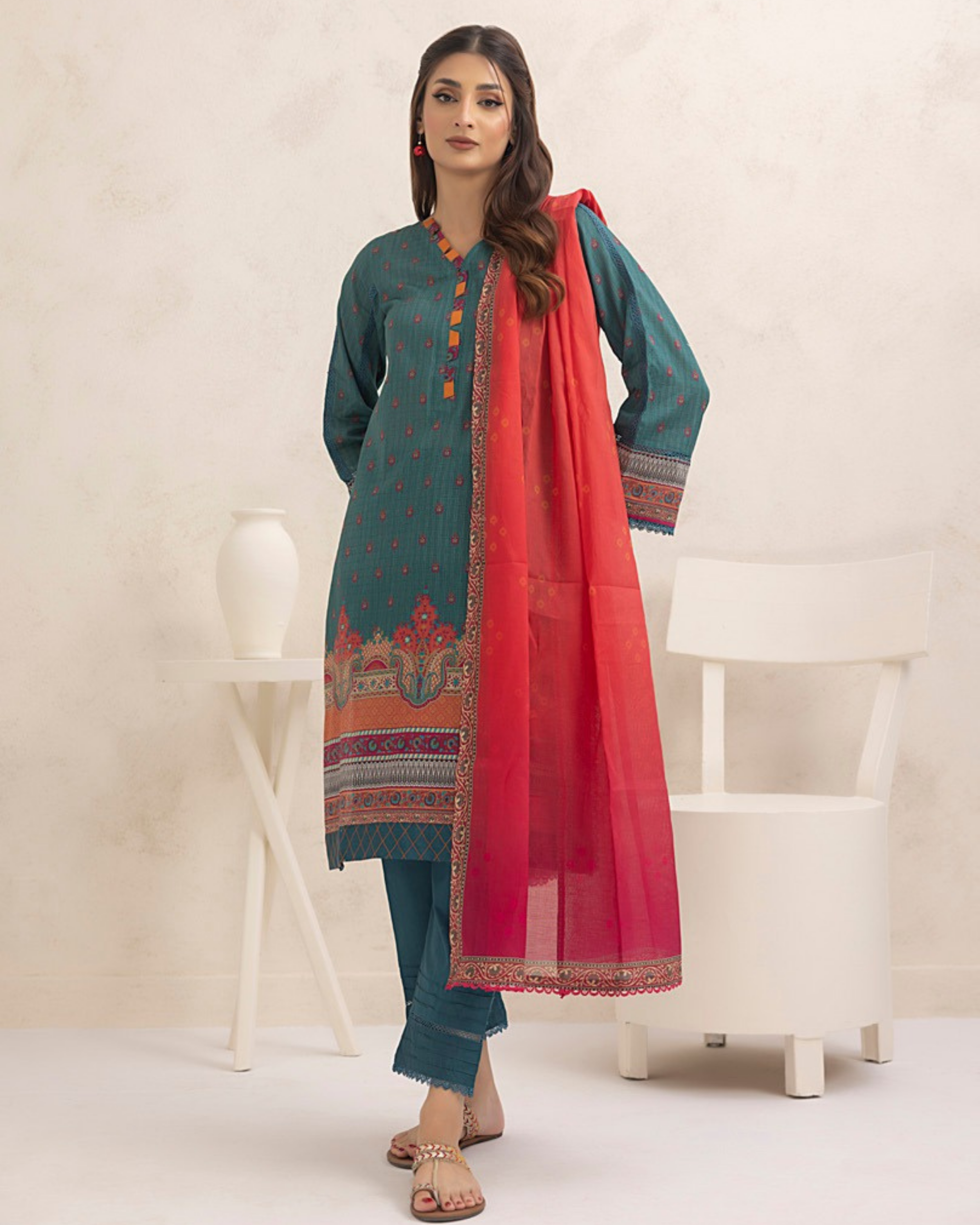 Woman wearing a teal outfit with a red dupatta in a minimalistic setting