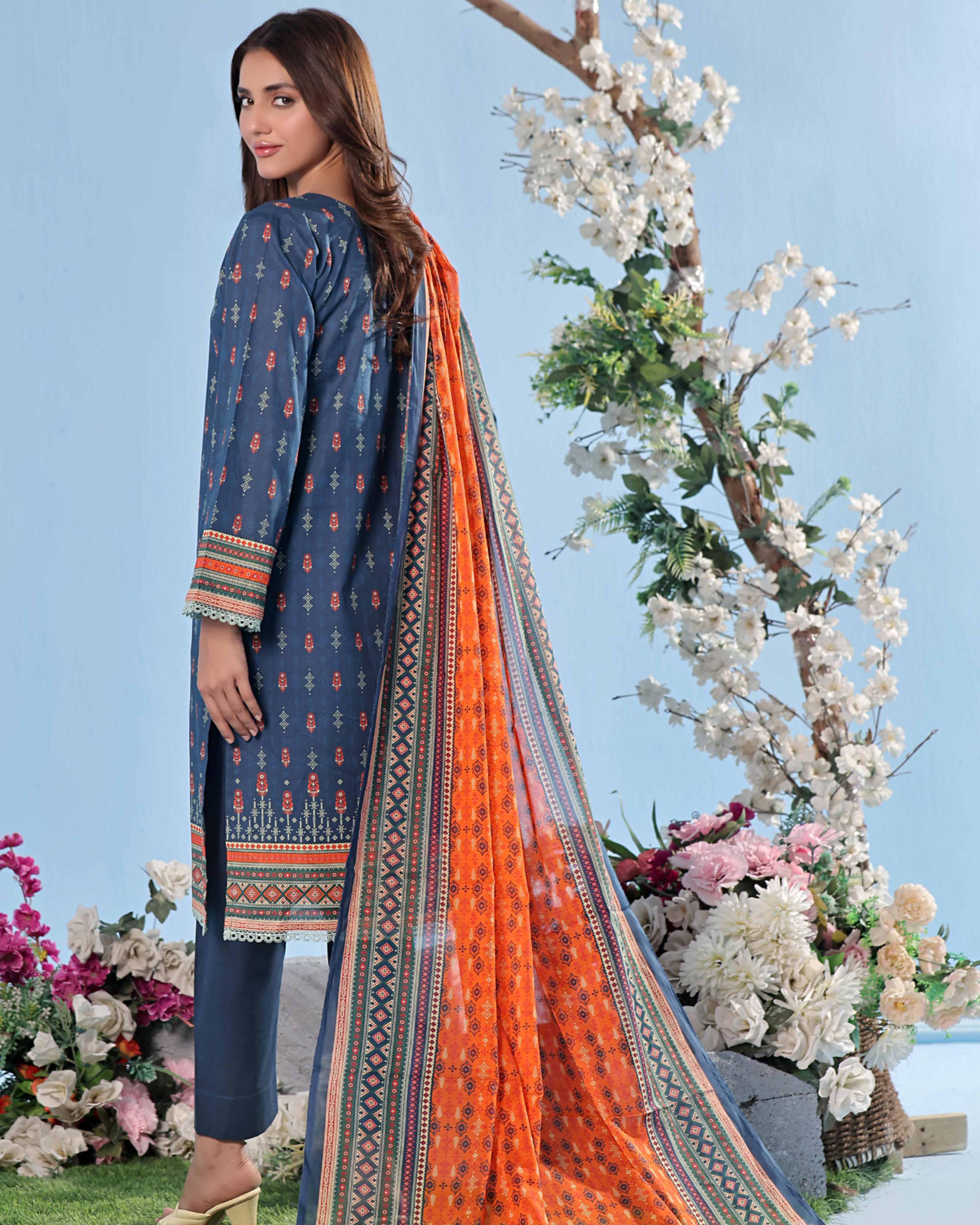 Woman wearing a blue and orange traditional outfit with a floral background