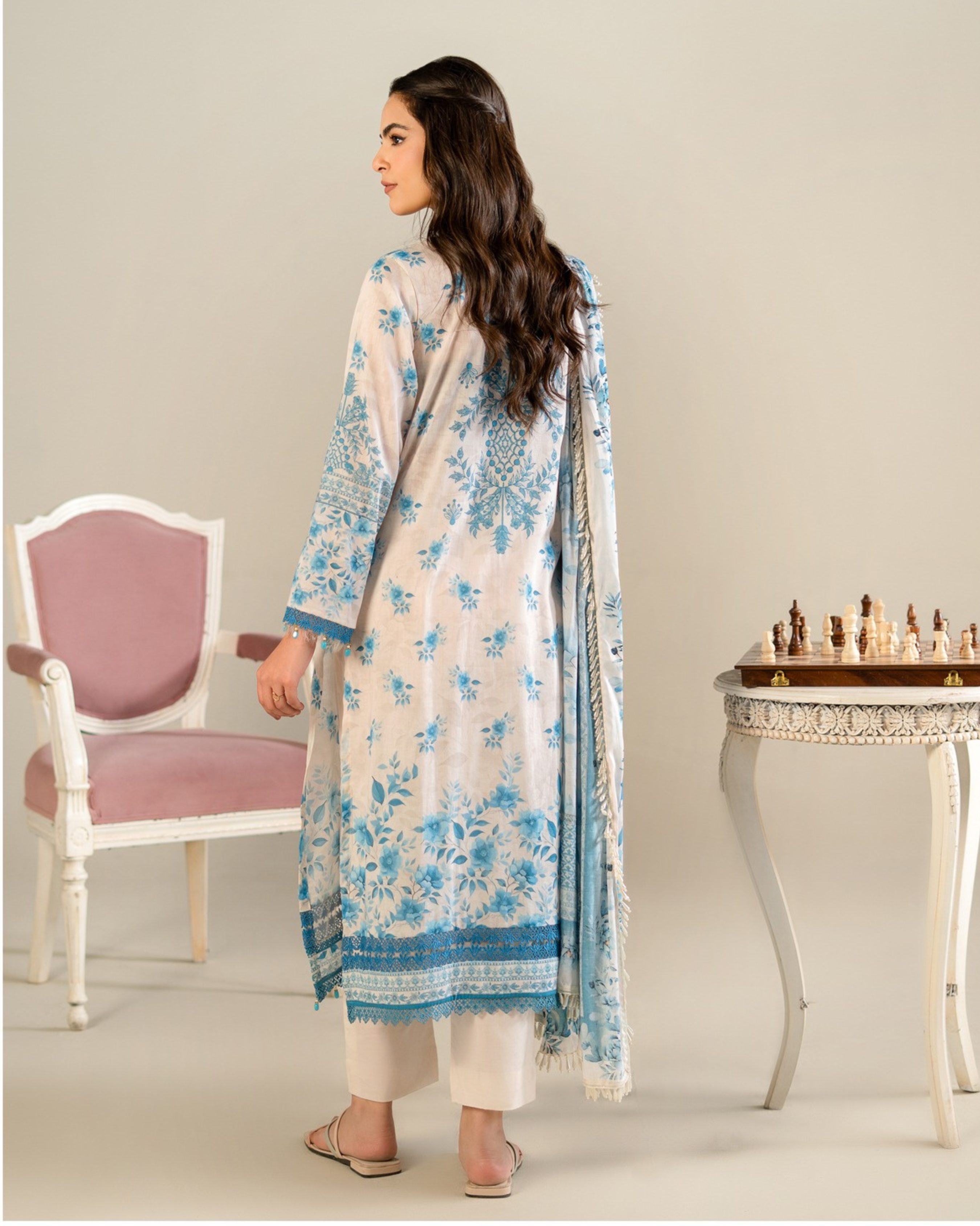 Woman wearing a floral dress standing in a room with a chair and chessboard.