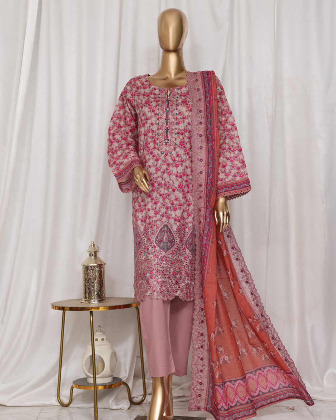 Mannequin wearing a pink and red patterned traditional outfit with a scarf on a white background