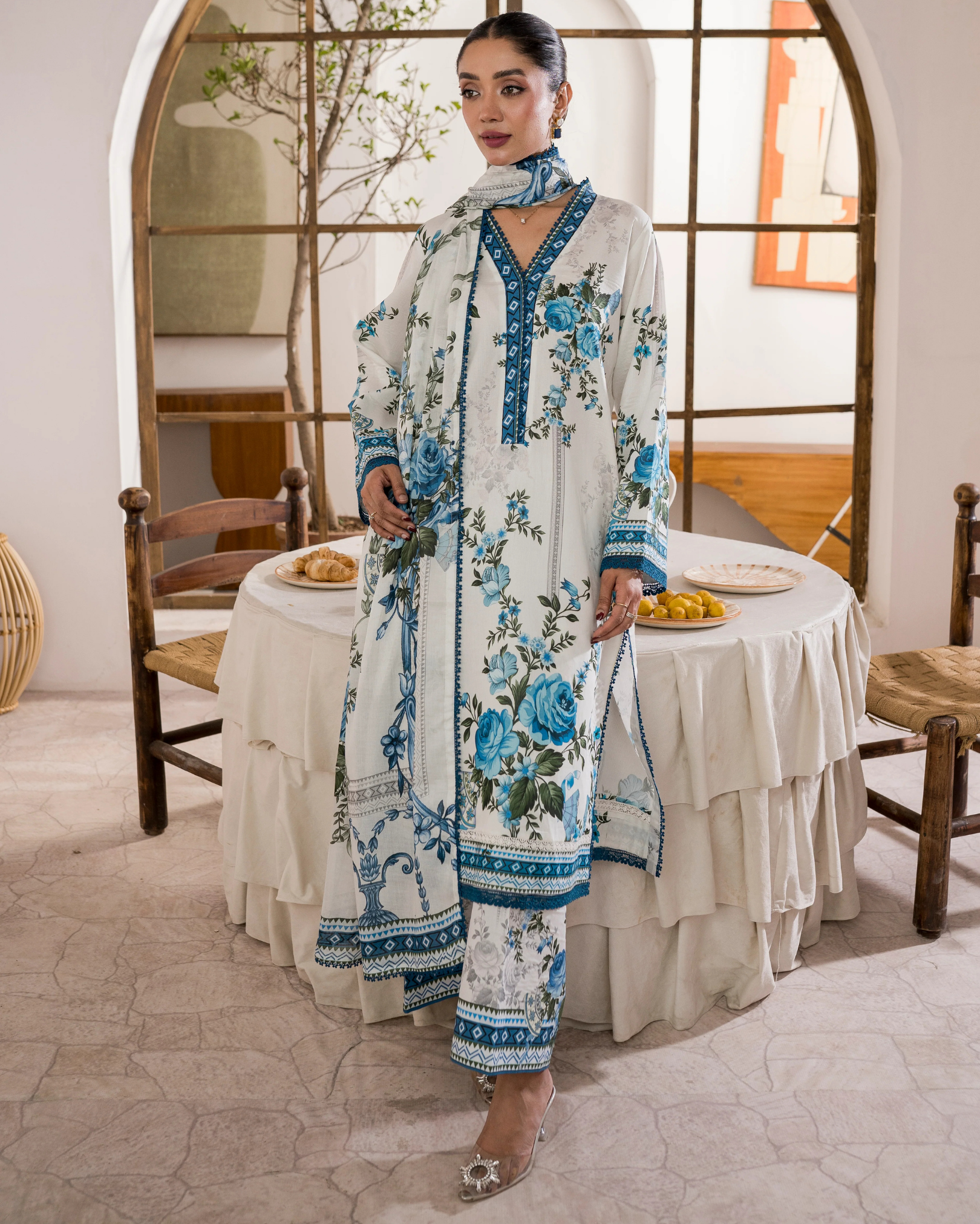 Woman in a floral dress standing in a dining area with a table and chairs.