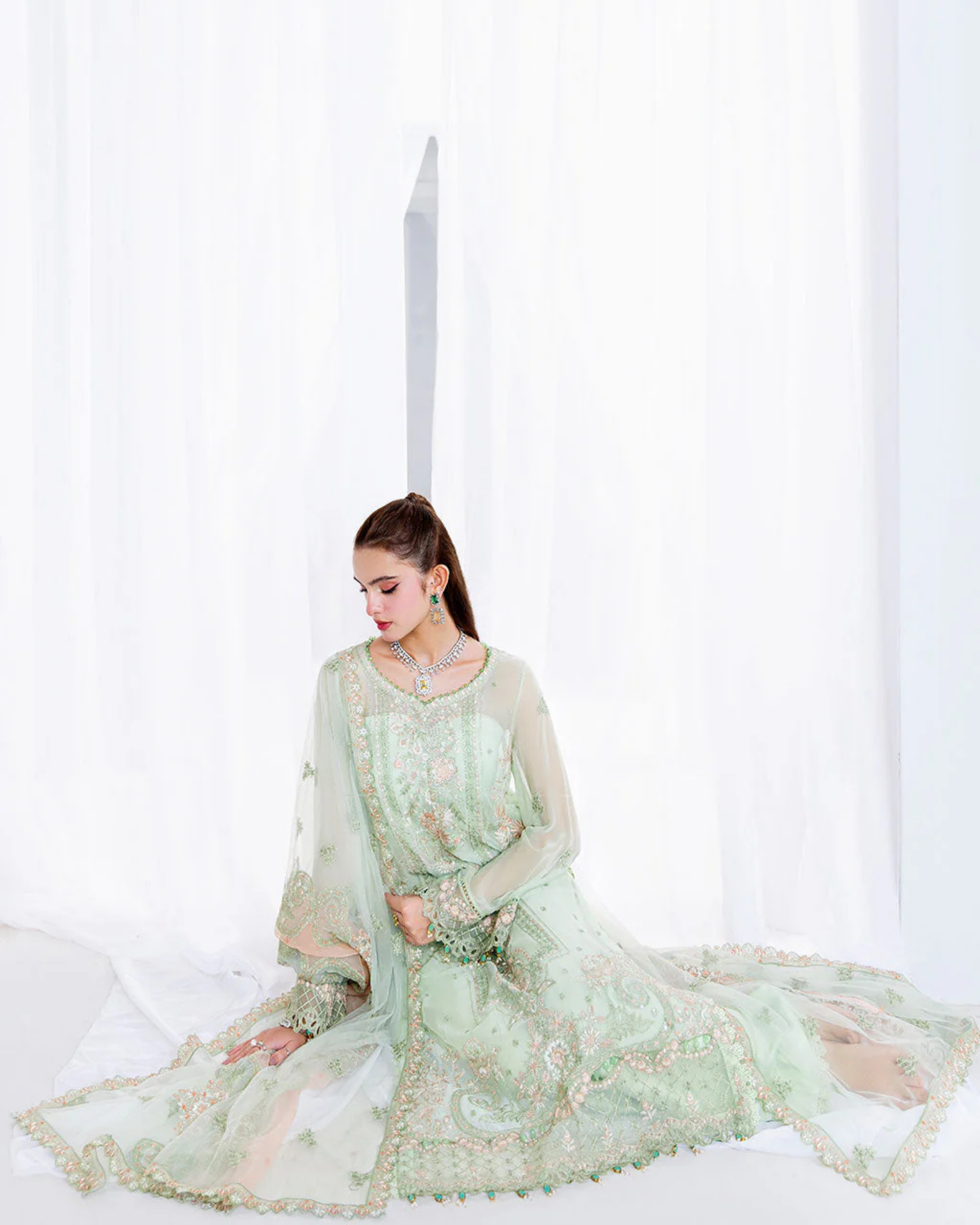 Woman in a light green traditional outfit sitting on a white surface with a white background