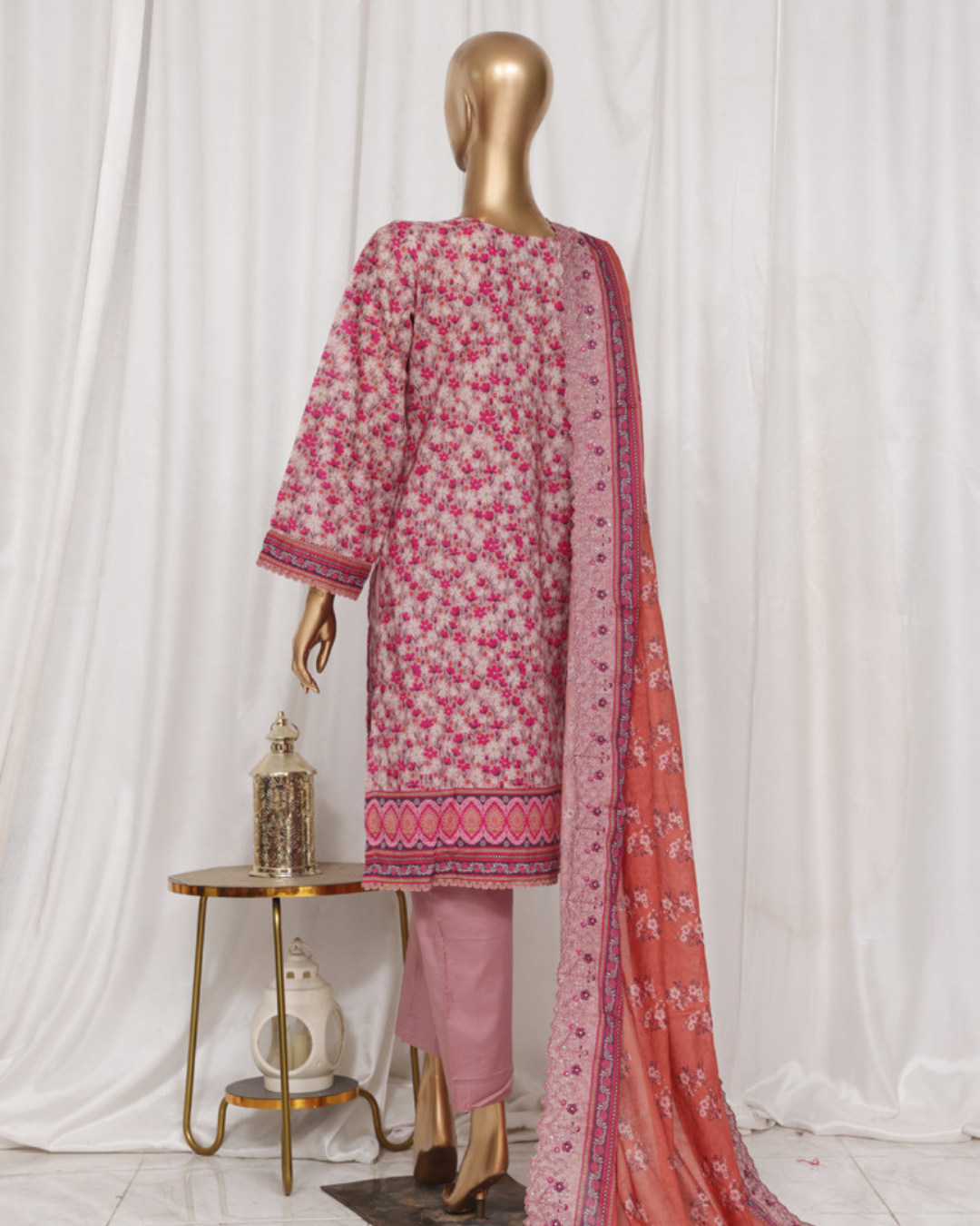 Mannequin wearing a pink and red floral outfit with a matching dupatta against a white curtain background.