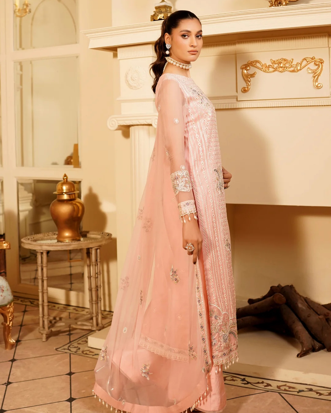 Woman in a light pink traditional outfit standing in an elegant room with decorative elements.