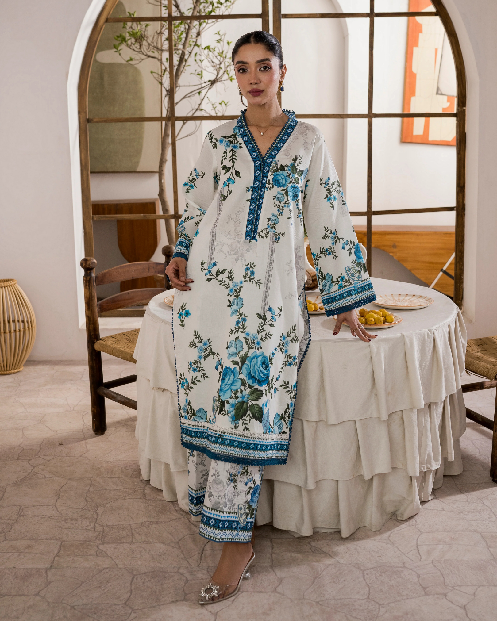 Woman in a floral dress standing in a room with a table and chairs.