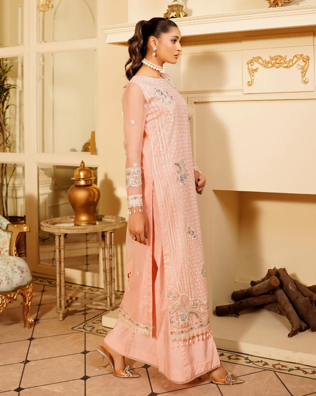 Woman in a pink traditional outfit standing in a decorated room with a fireplace.