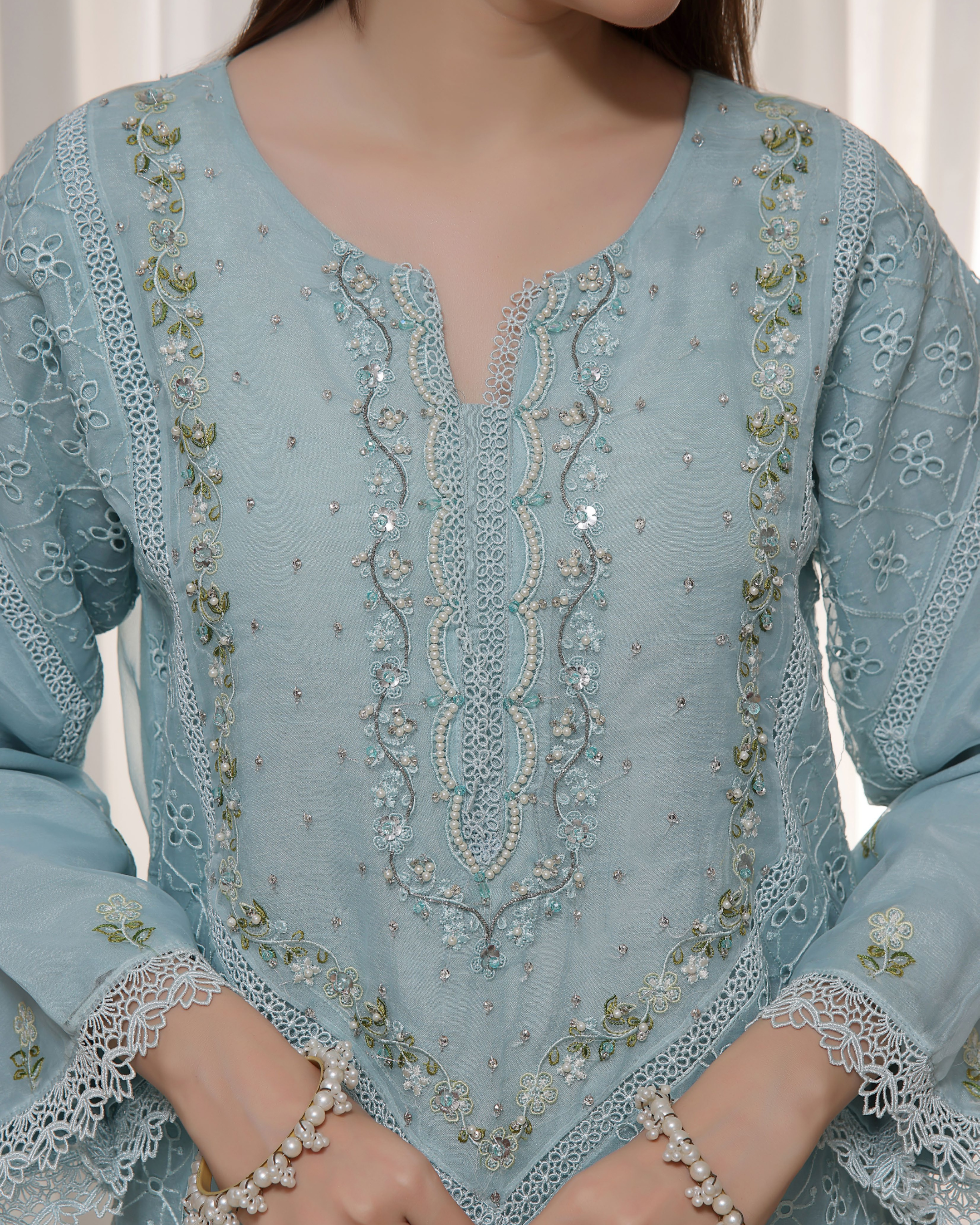 Light blue embroidered garment with intricate patterns on a neutral background