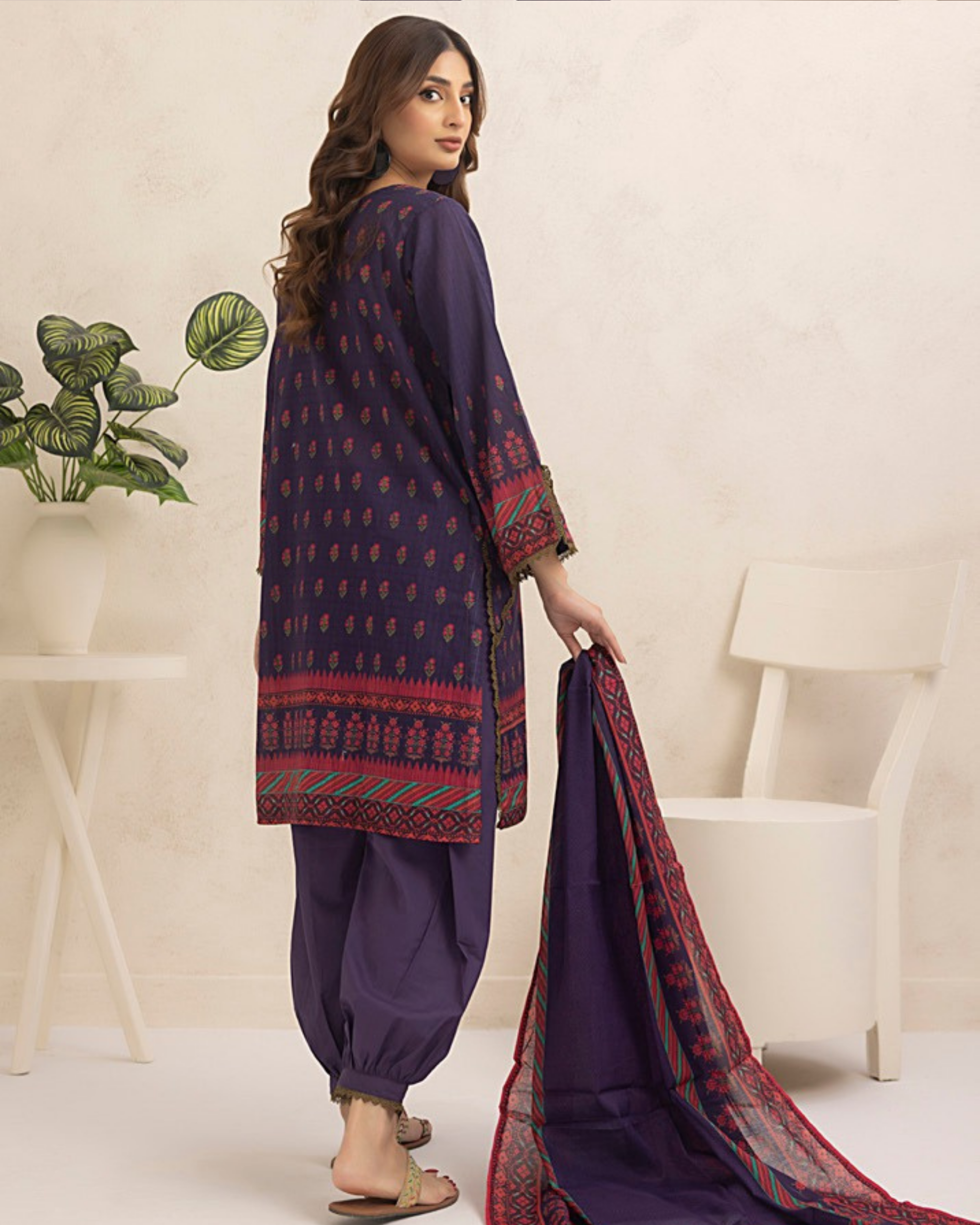 Woman wearing a traditional outfit with intricate patterns in a minimalistic setting.