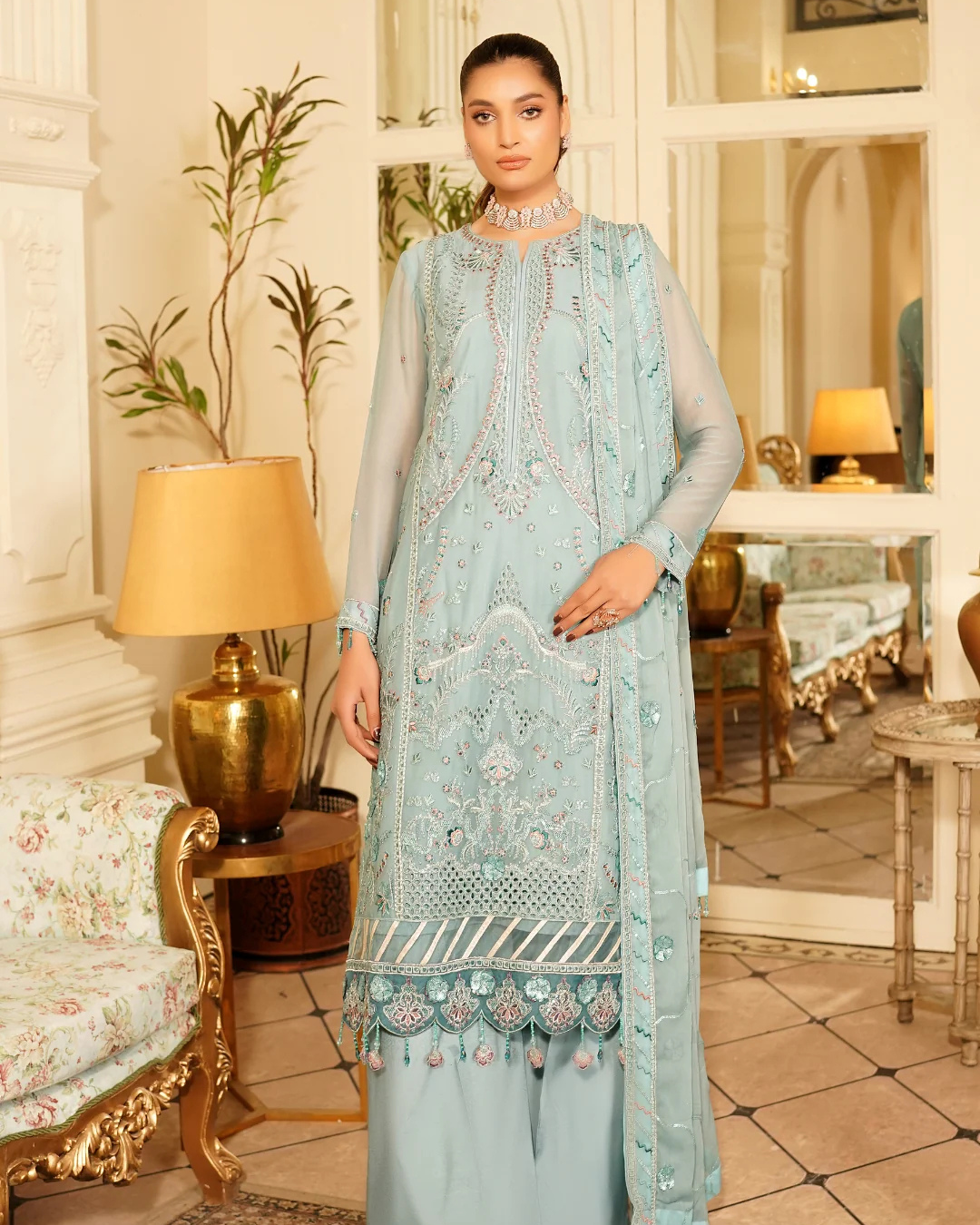 Woman wearing a light blue embroidered traditional outfit in an elegant room.