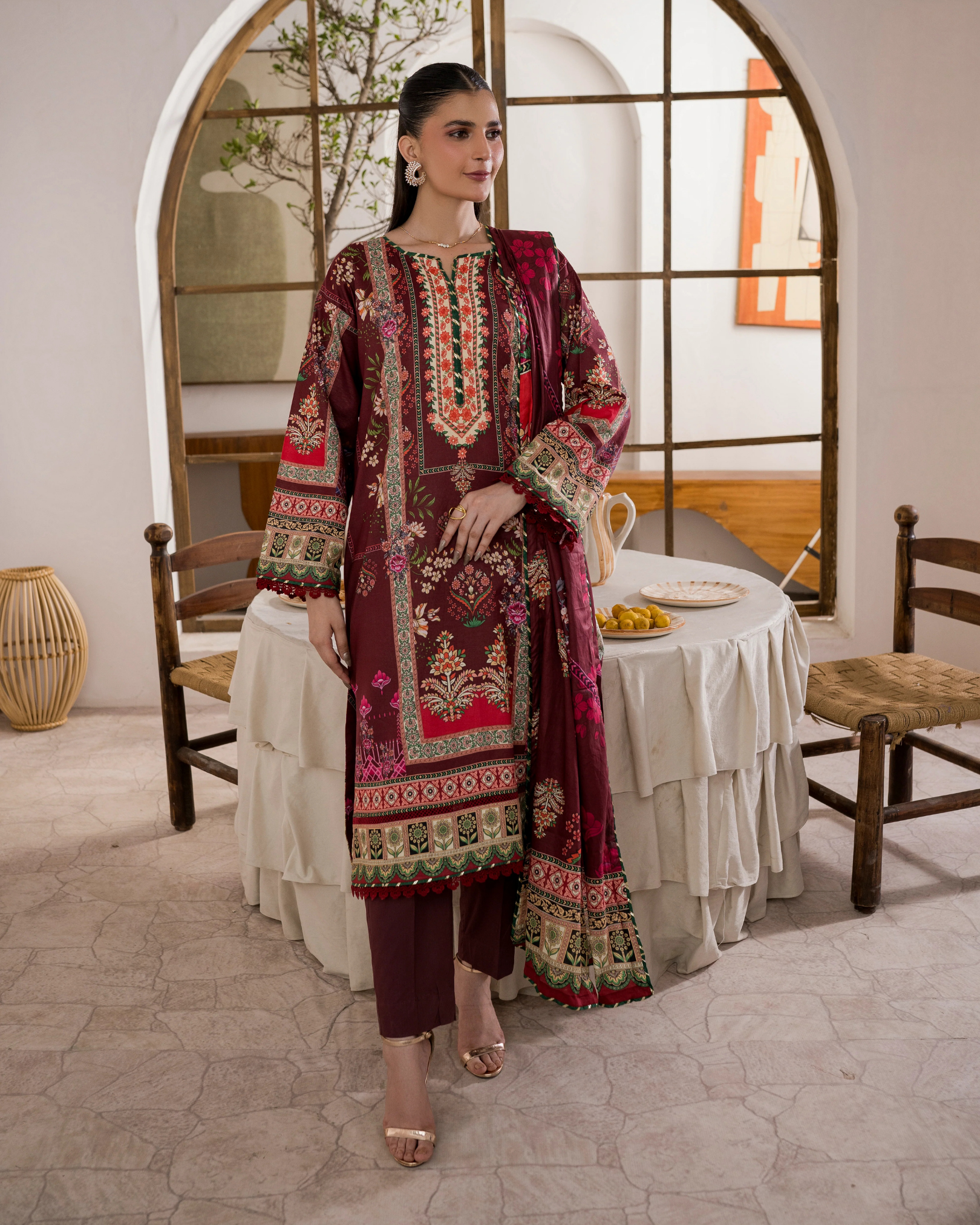 Woman in a patterned dress standing in a room with a mirror and table.