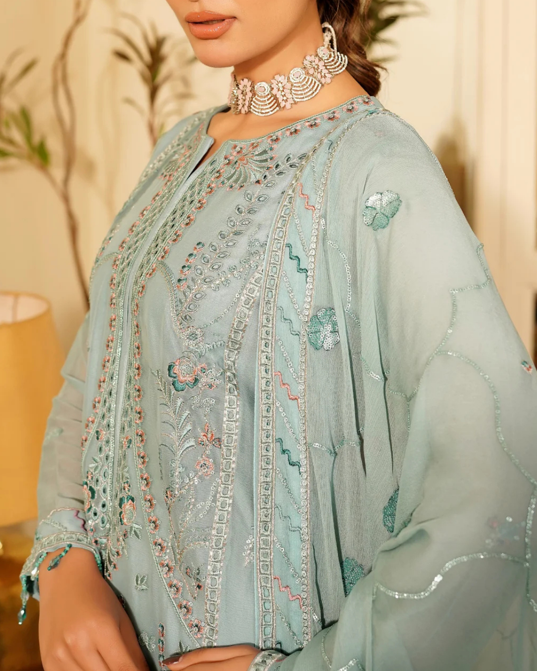 Light blue embroidered traditional outfit with a necklace against a blurred indoor background