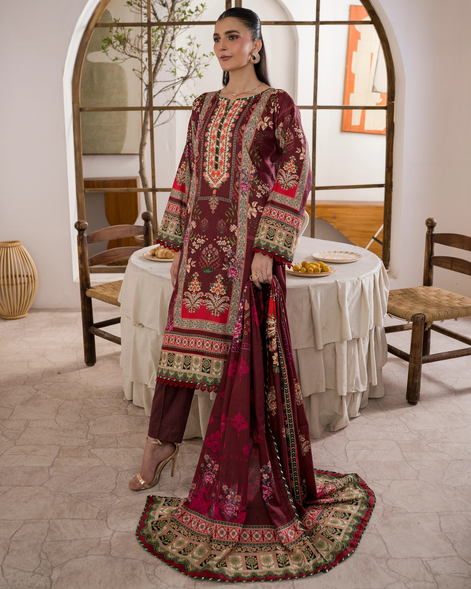 Woman in a traditional embroidered outfit standing in a room with a table and chairs.