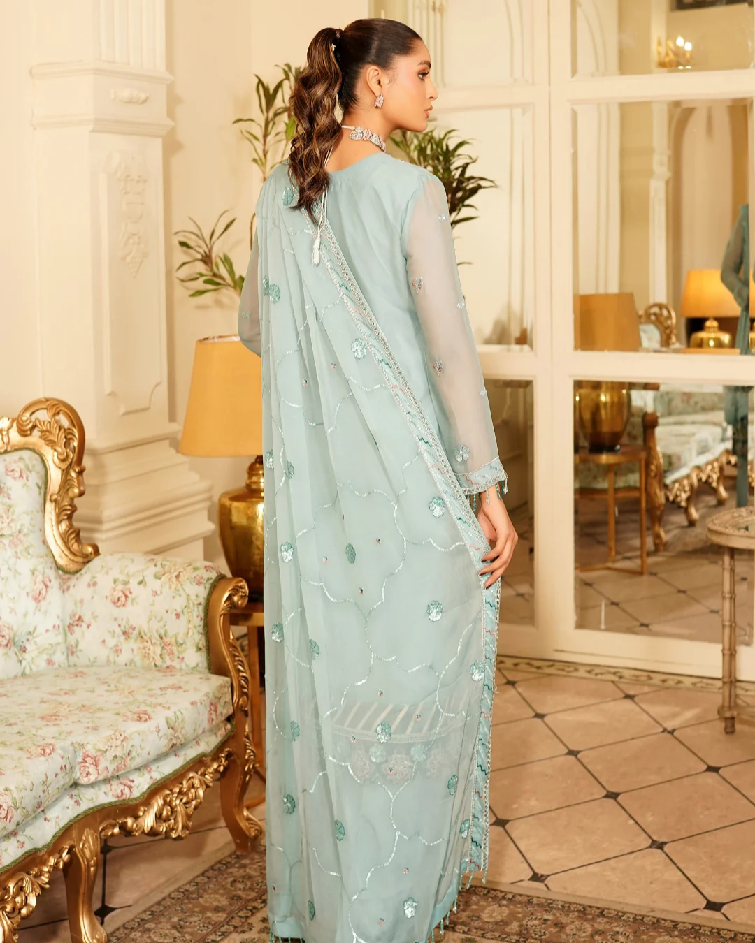 Woman in a light blue saree with a floral pattern in an elegant room.