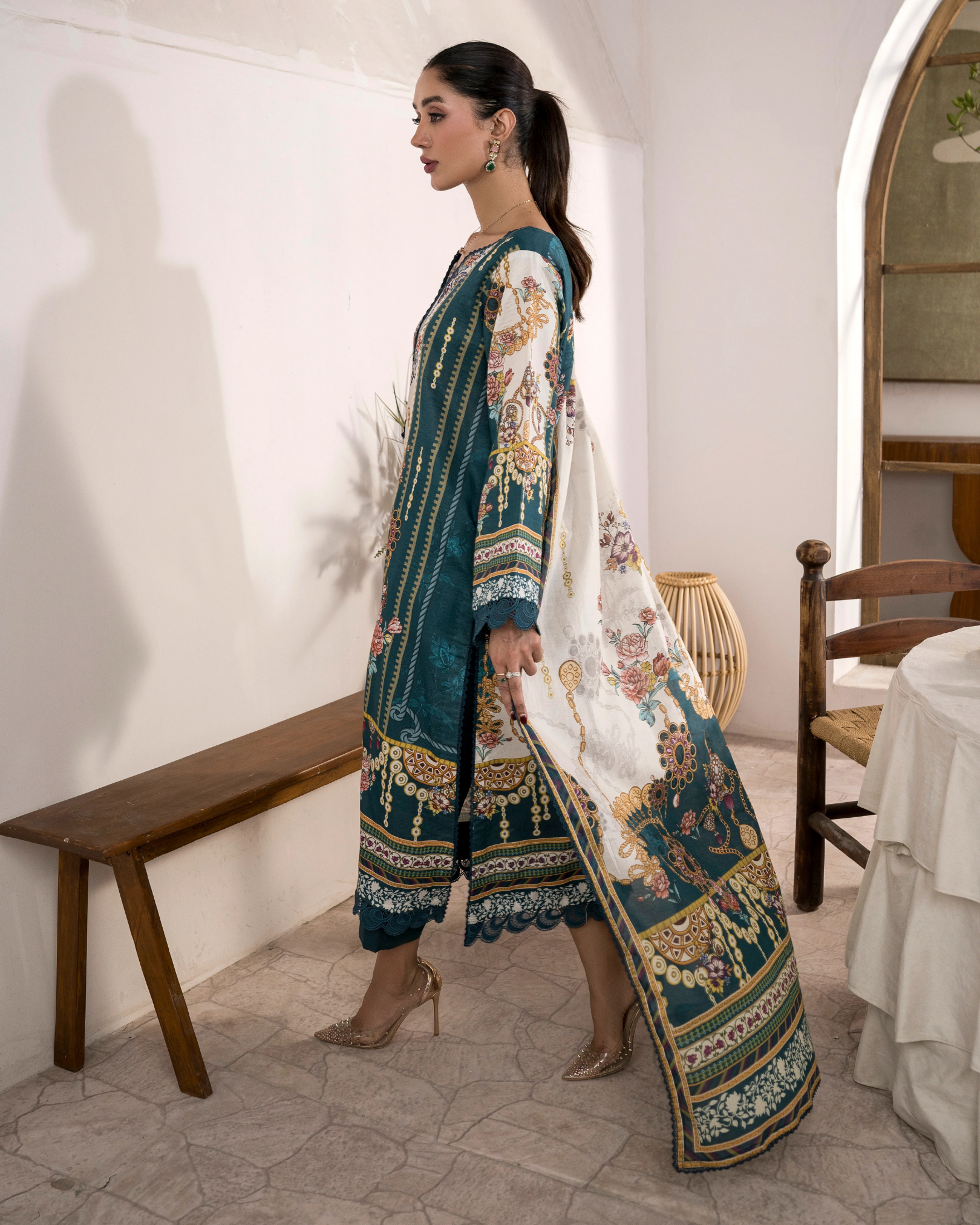 Woman in a traditional outfit with floral patterns walking in a room with wooden furniture.