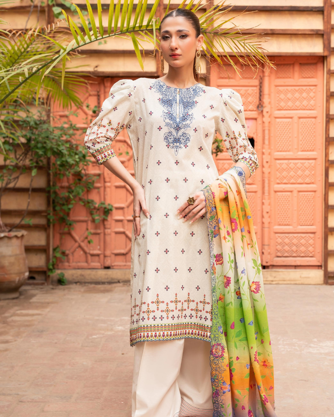 Woman in a traditional outfit with a colorful dupatta standing in front of a textured wall.